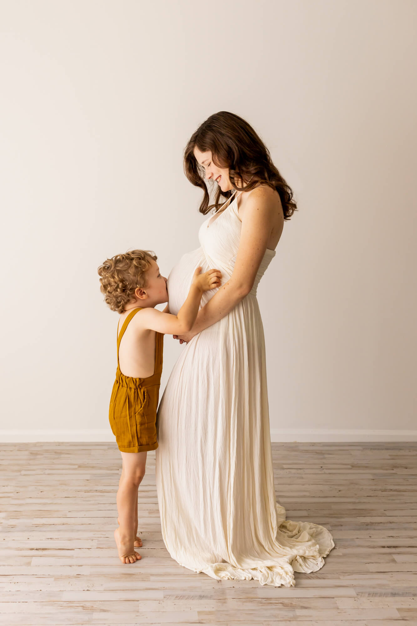 pregnant mom in cream gown with son kissing her belly