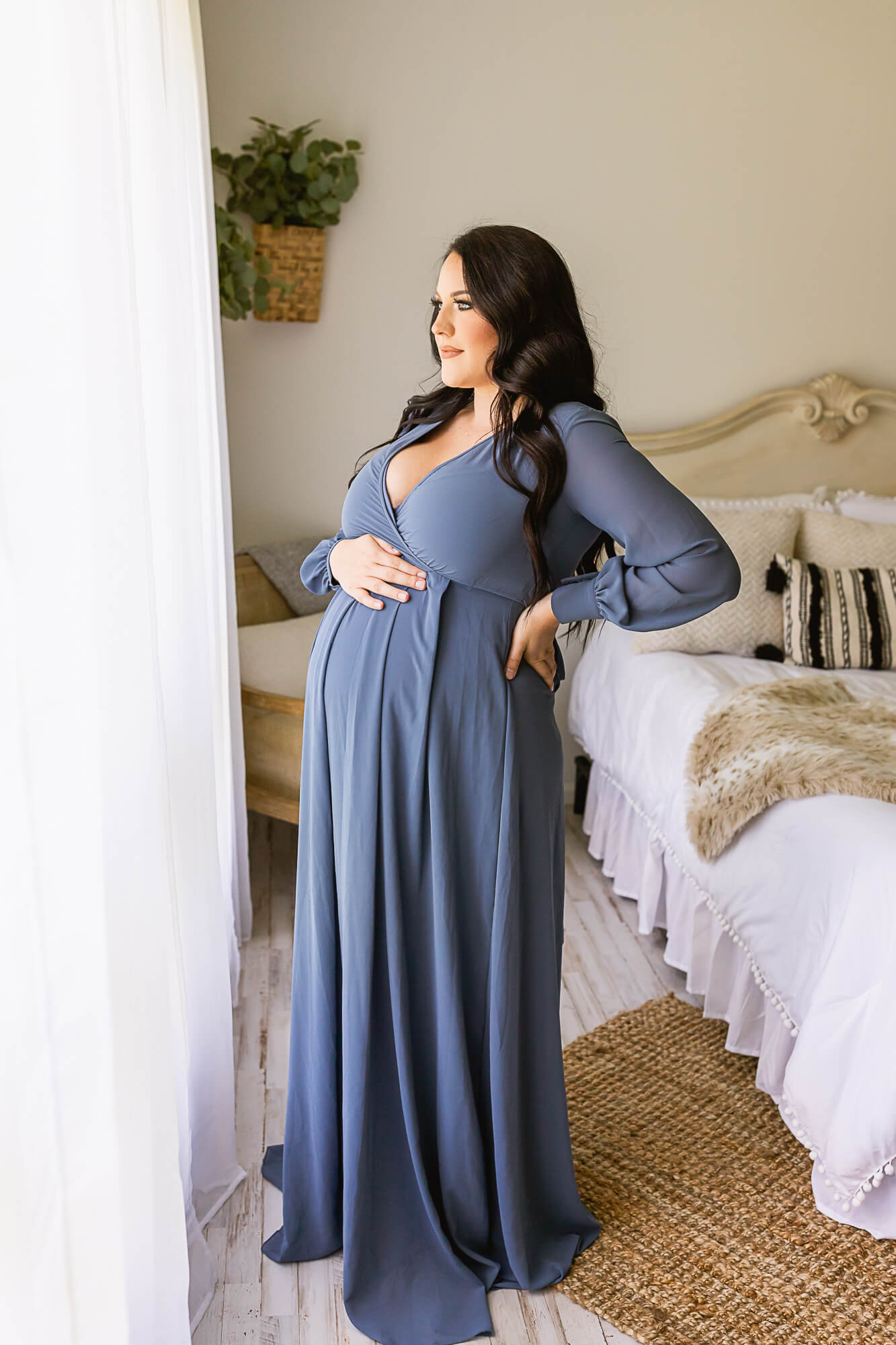 Expectant mom in blue gown holding her bump and looking out the window Birmingham Doula