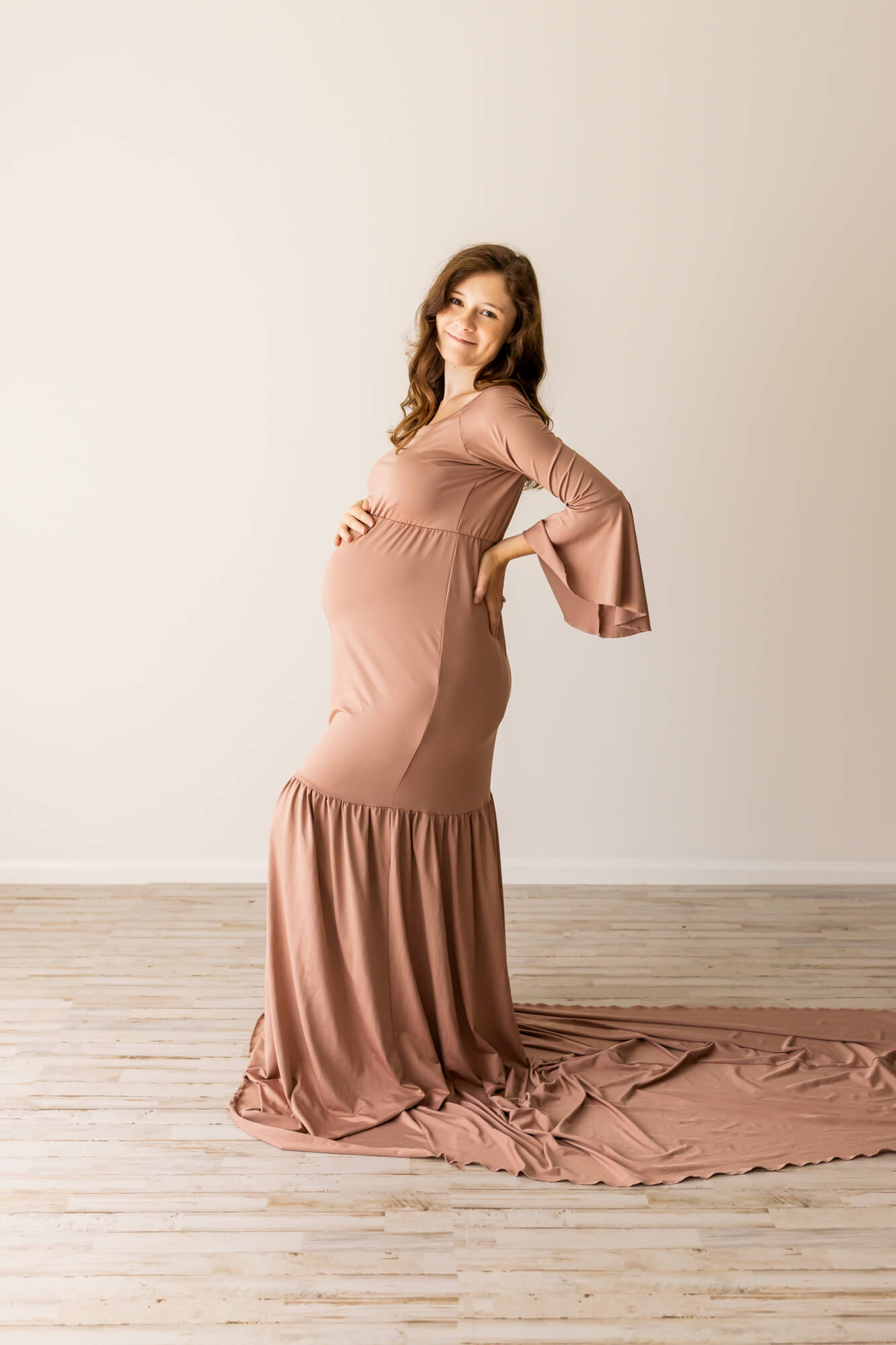 mom to be in brown gown resting her hands on her belly and back birmingham prenatal massage