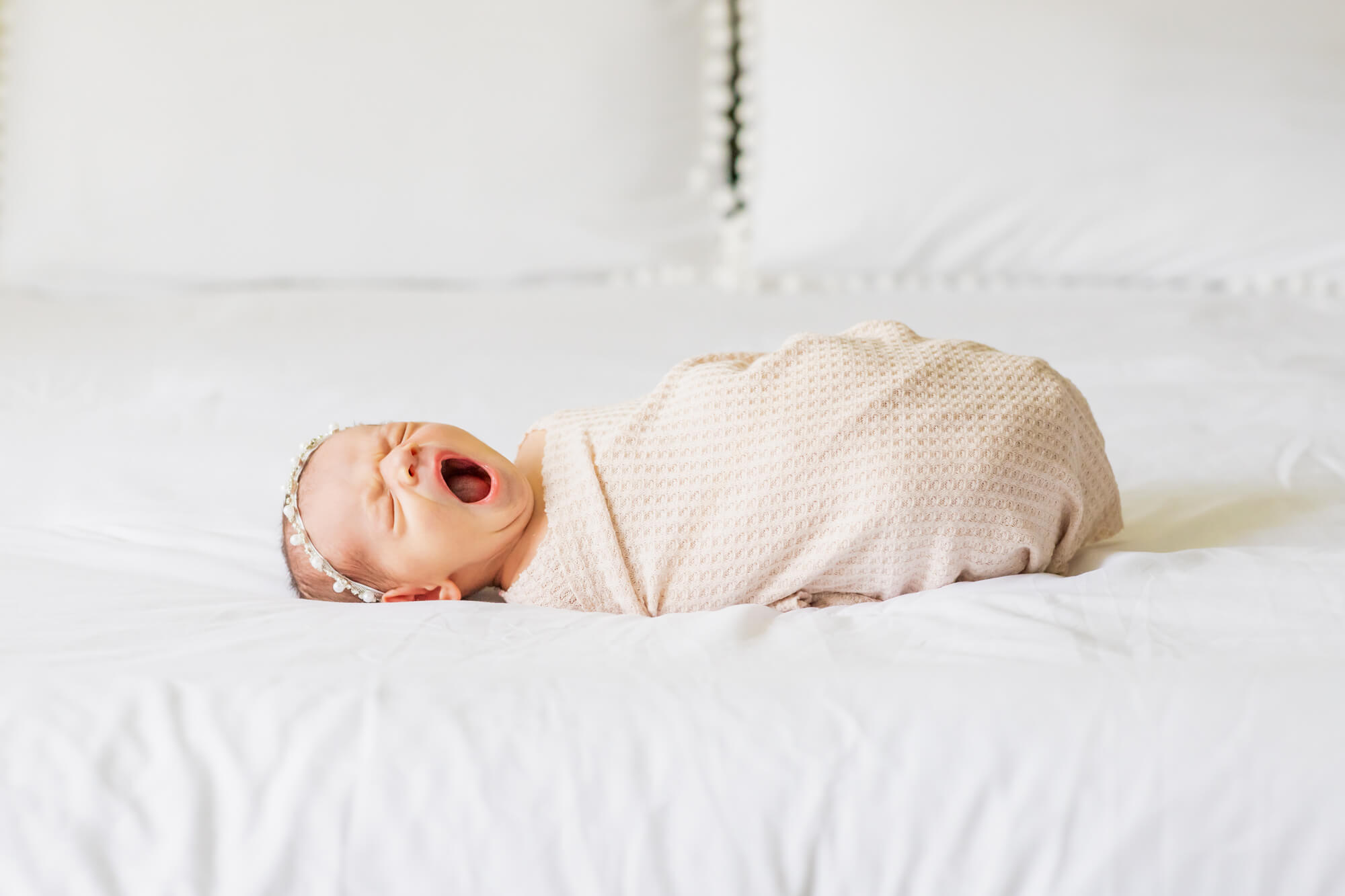 newborn baby wrapped in neutral colors yawning on a bed Water Birth Birmingham AL