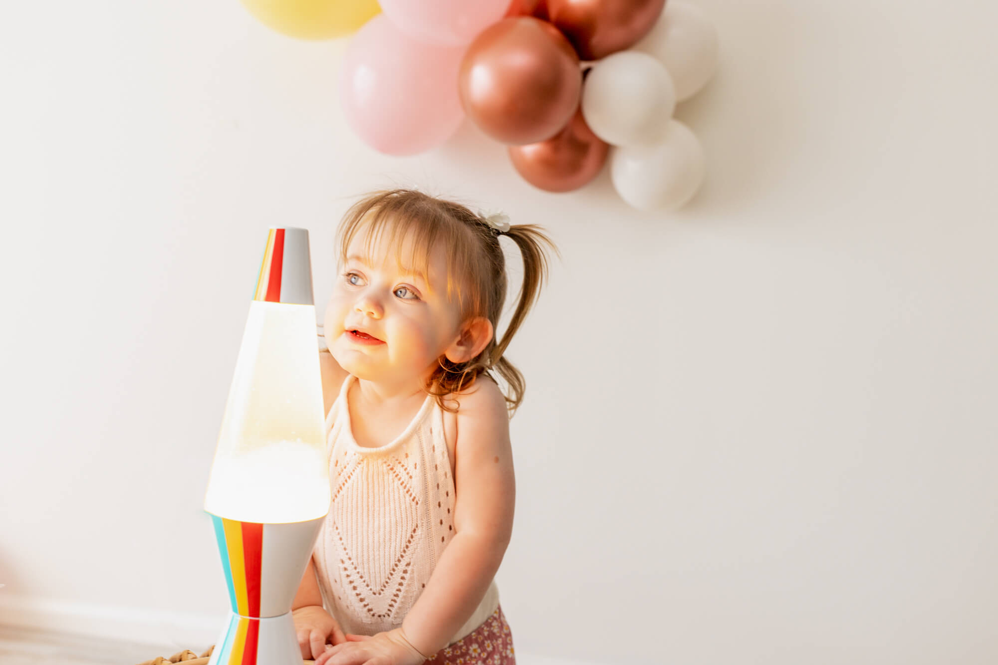 little girl in white shirt and pigtails looking at a lava lamp