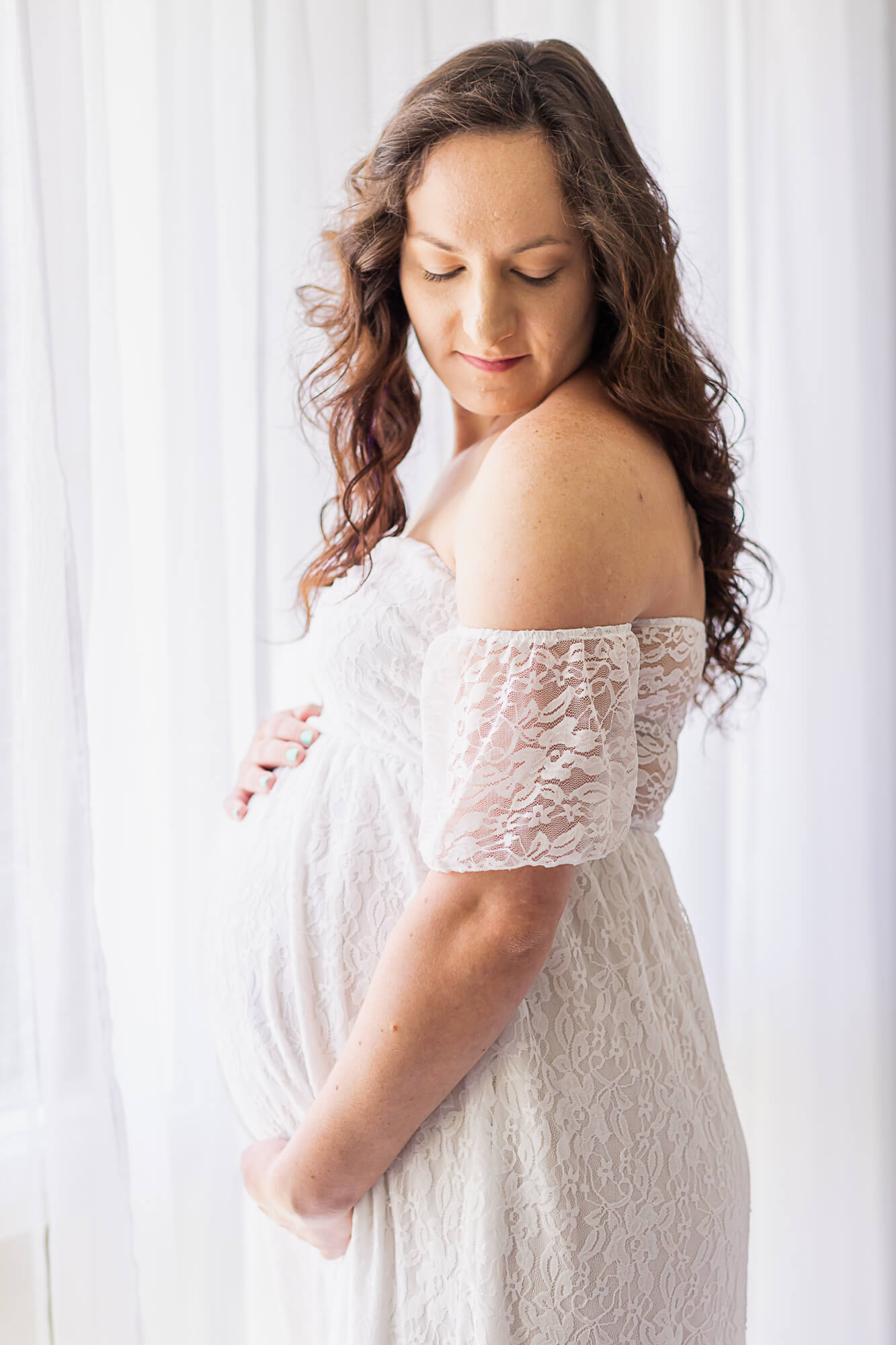 mom to be in white off the shoulder gown standing near a window 4D Ultrasound Birmingham AL
