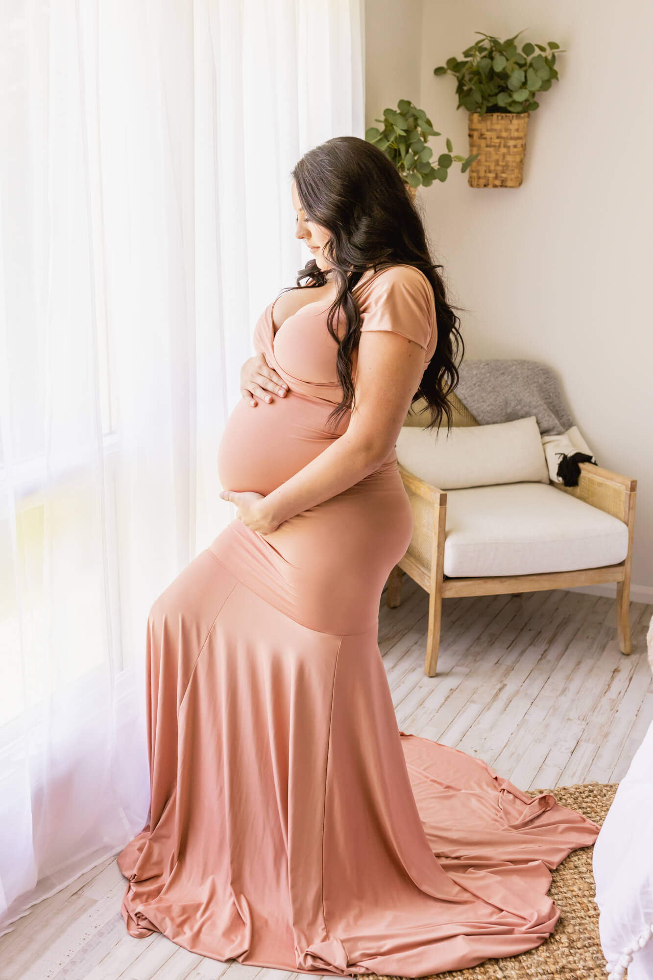 Mom to be in pink gown standing near a window holding her bump alabama fertility specialists