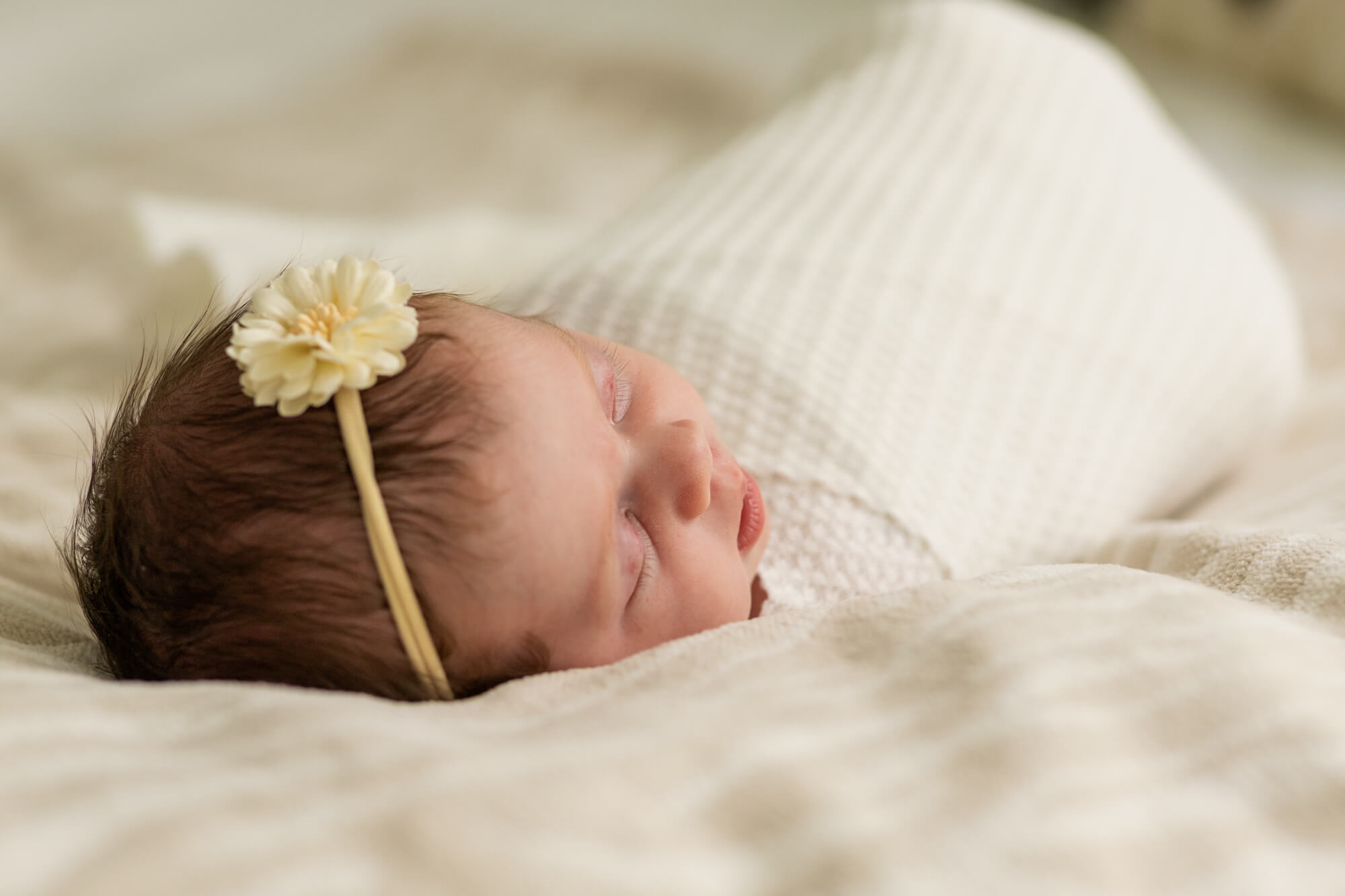 Newborn baby girl in cream swaddle and flower headband Eastern OBGYN
