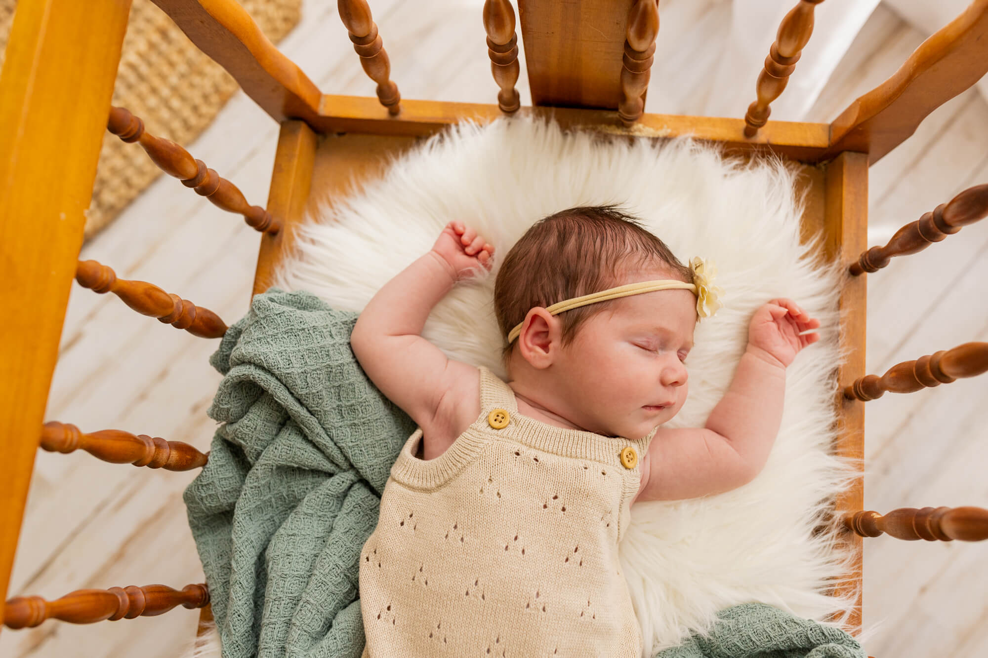 newborn baby girl in cream onesie and headband sleeping with arms up