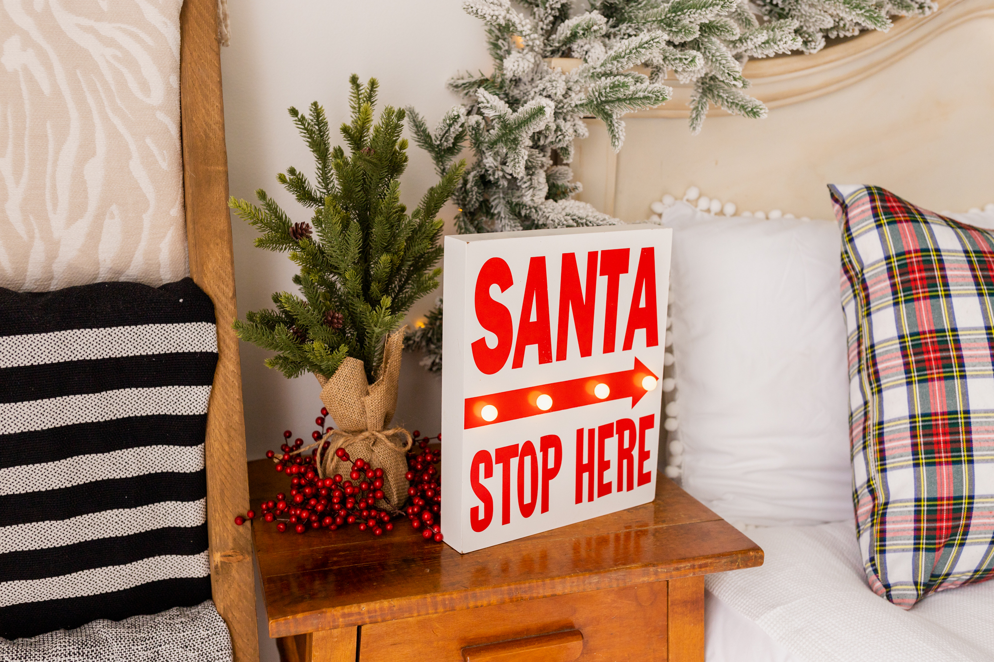 Christmas sign Santa stop here on an end table beside a bed
