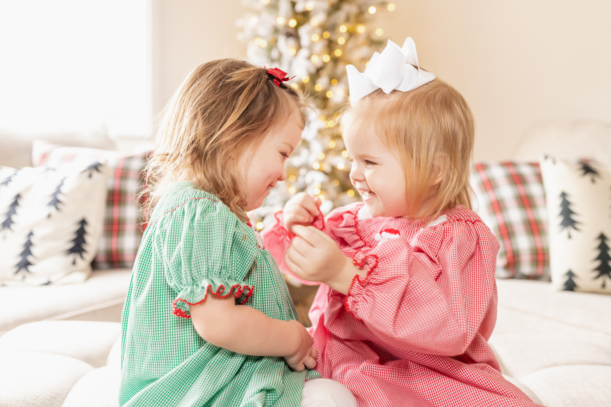 Toddler girls in smocked dresses playing in front of a Christmas tree