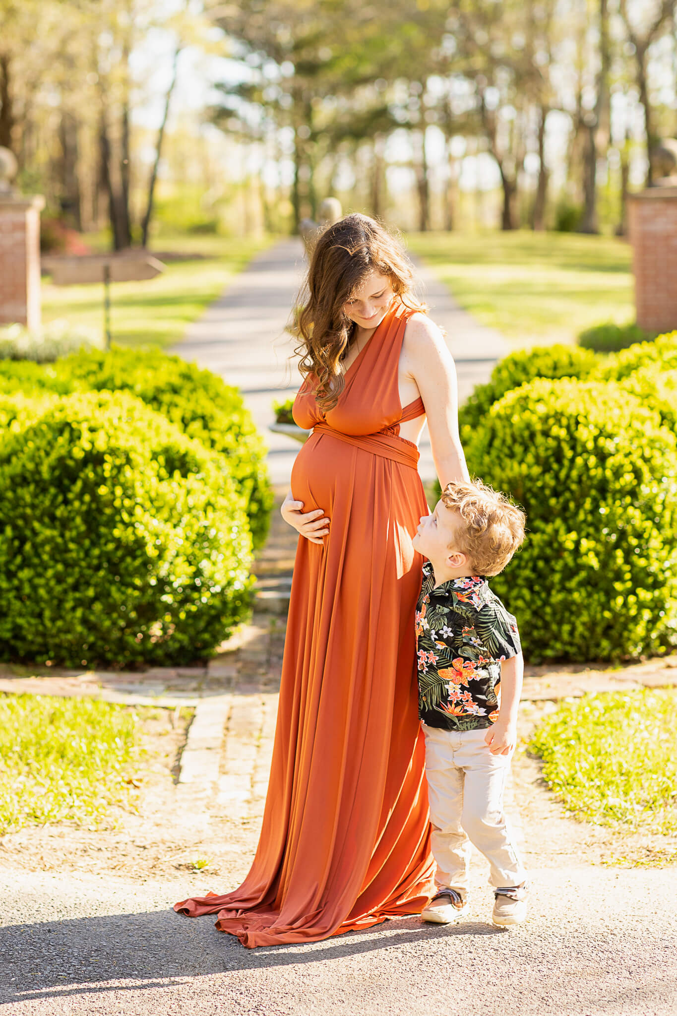 Mom to be in orange gown holding her bump and looking at her toddler Earthkeeper Yoga