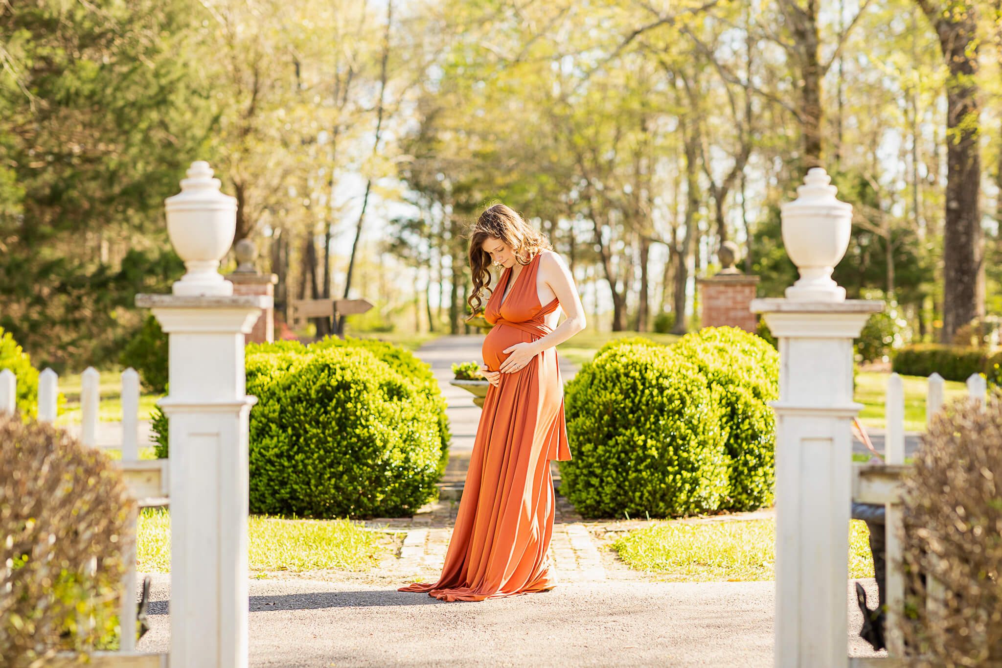 mom to be in orange gown looking down at her bump in a garden Earthkeeper Yoga