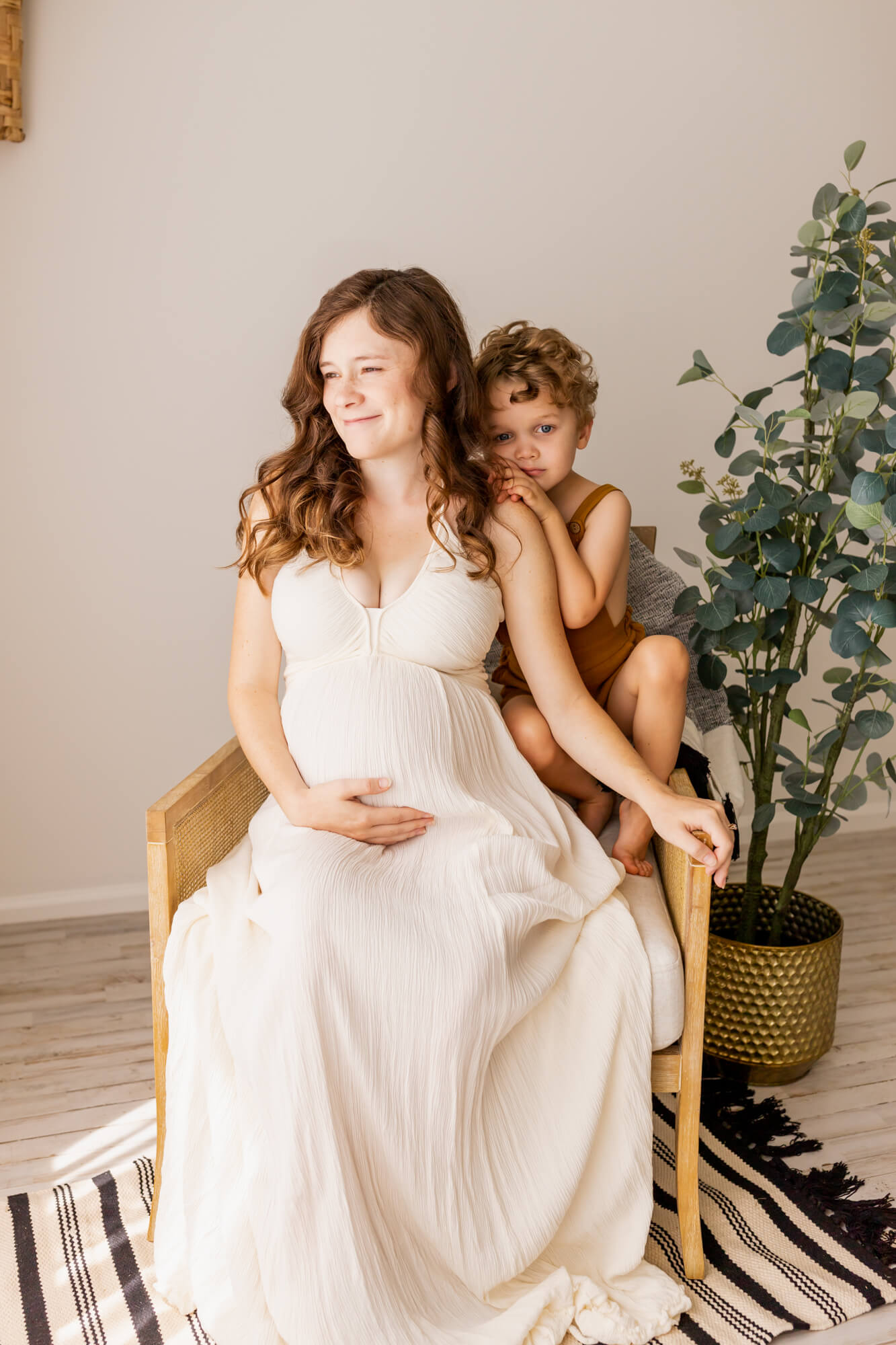pregnant woman in white maternity gown sitting in a chair with her son hugging her shoulder