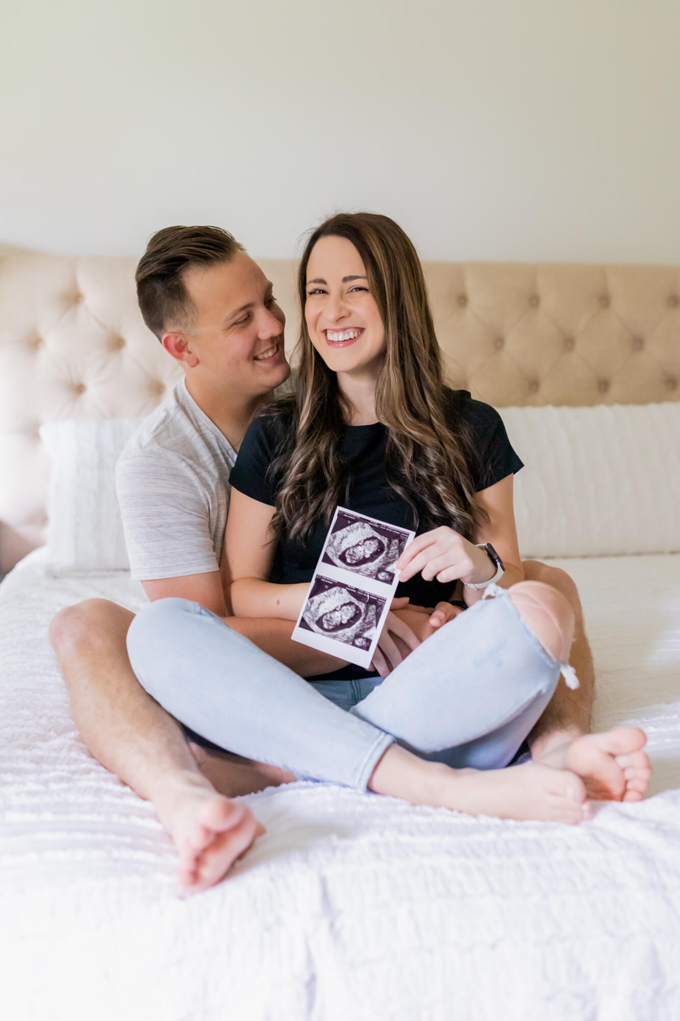 mom and dad to be sitting on a bed with their ultrasound Sharp and Stone OBGYN