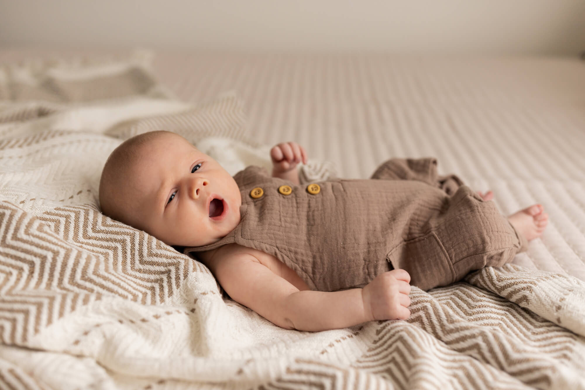 newborn baby in brown onesie laying on a bed storkland baby