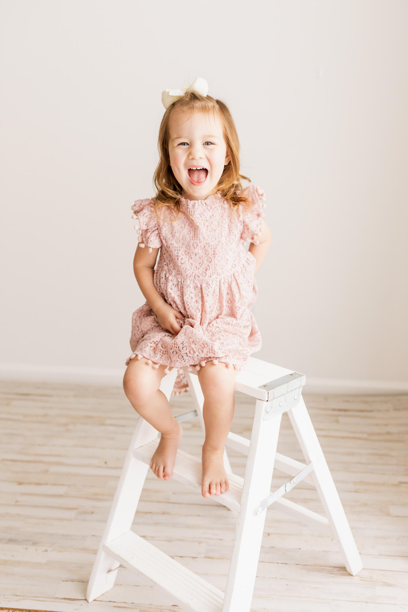 Young girl plays on top of a white step ladder in a pink dress