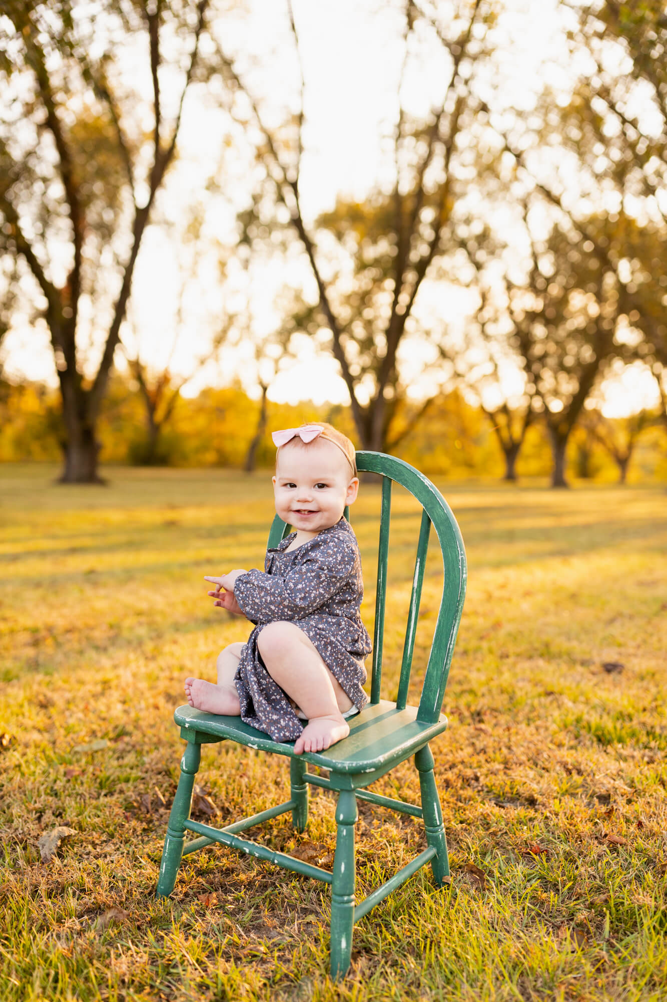 Toddler sits on a green wooden chair in a field