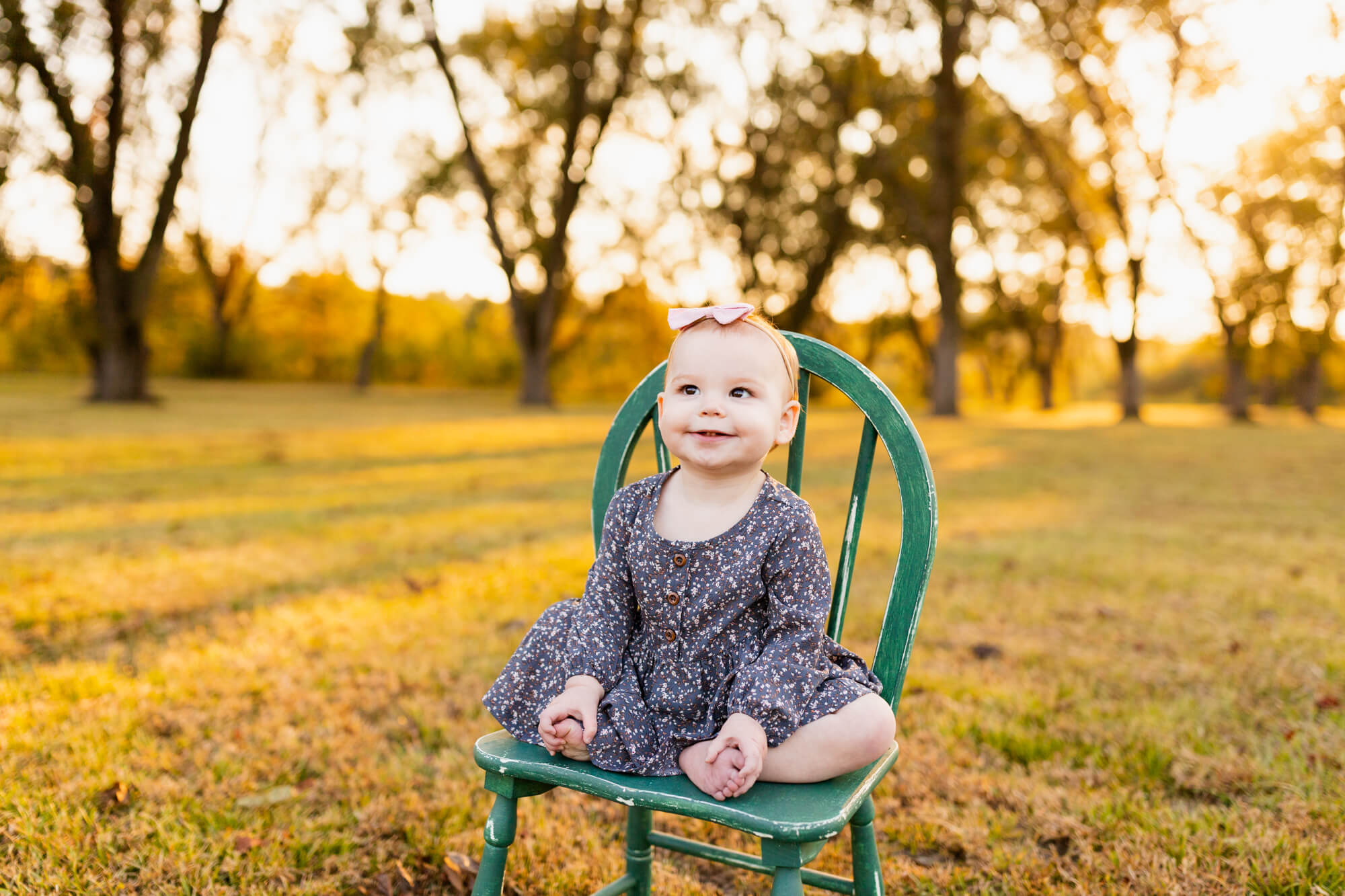 Toddler sits wearing a blue dress in a green wooden chair in a golden field turquoise boutique hoover al