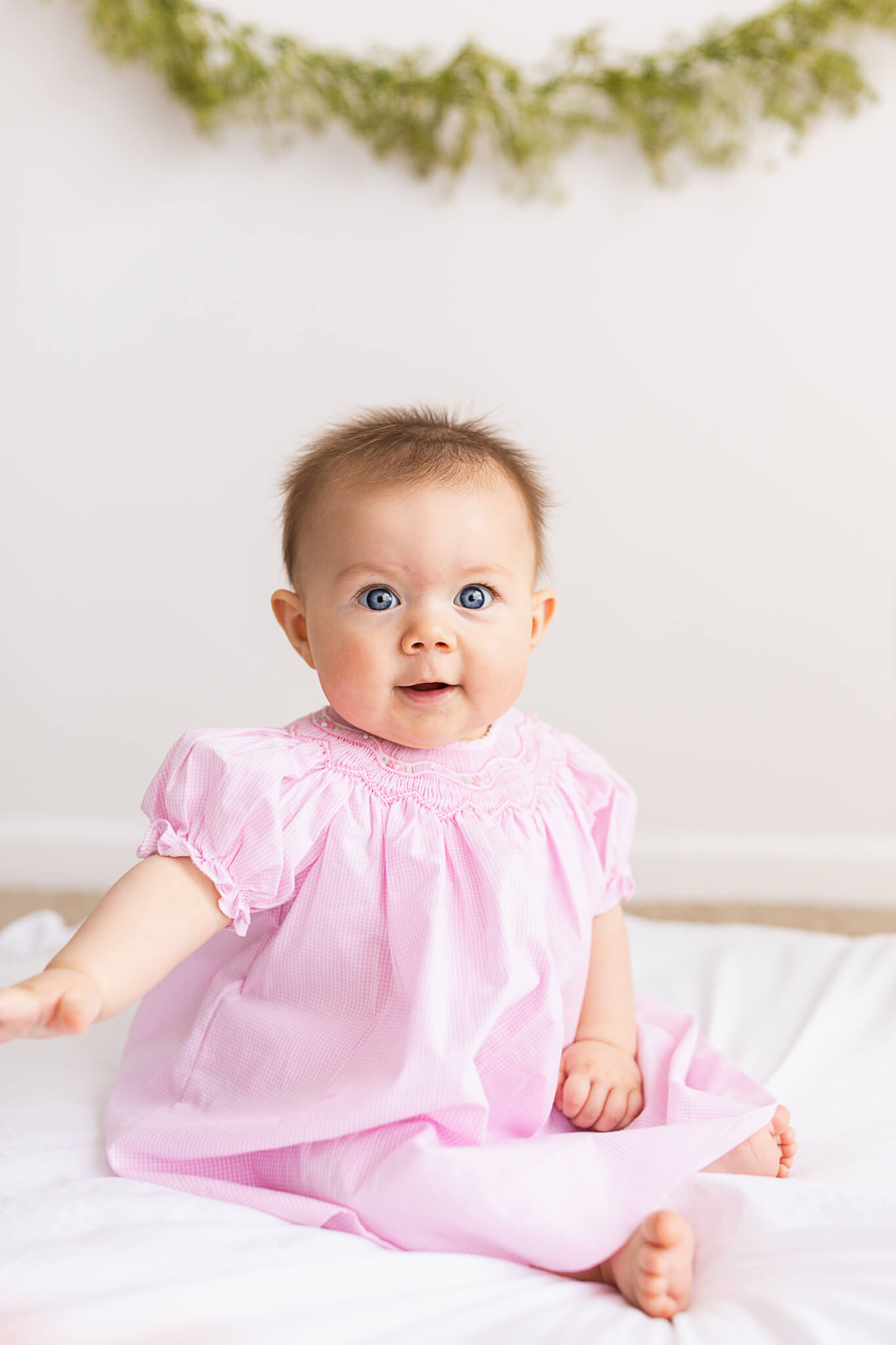Toddler in a pink ruffled dress sits on a mat in a studio Marlee Jane's