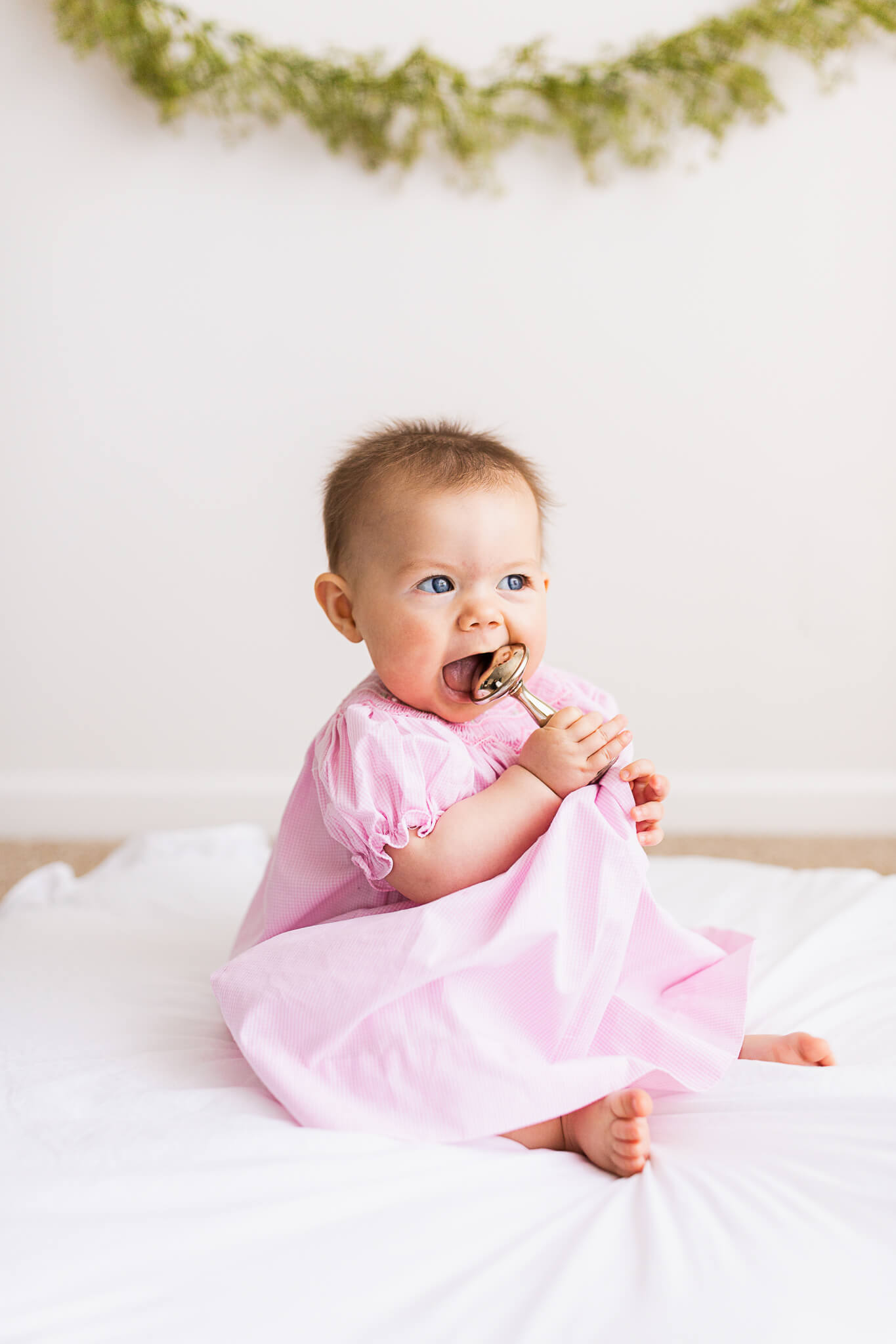 Toddler in a pink dress chews on a rattle toy in a studio Marlee Jane's