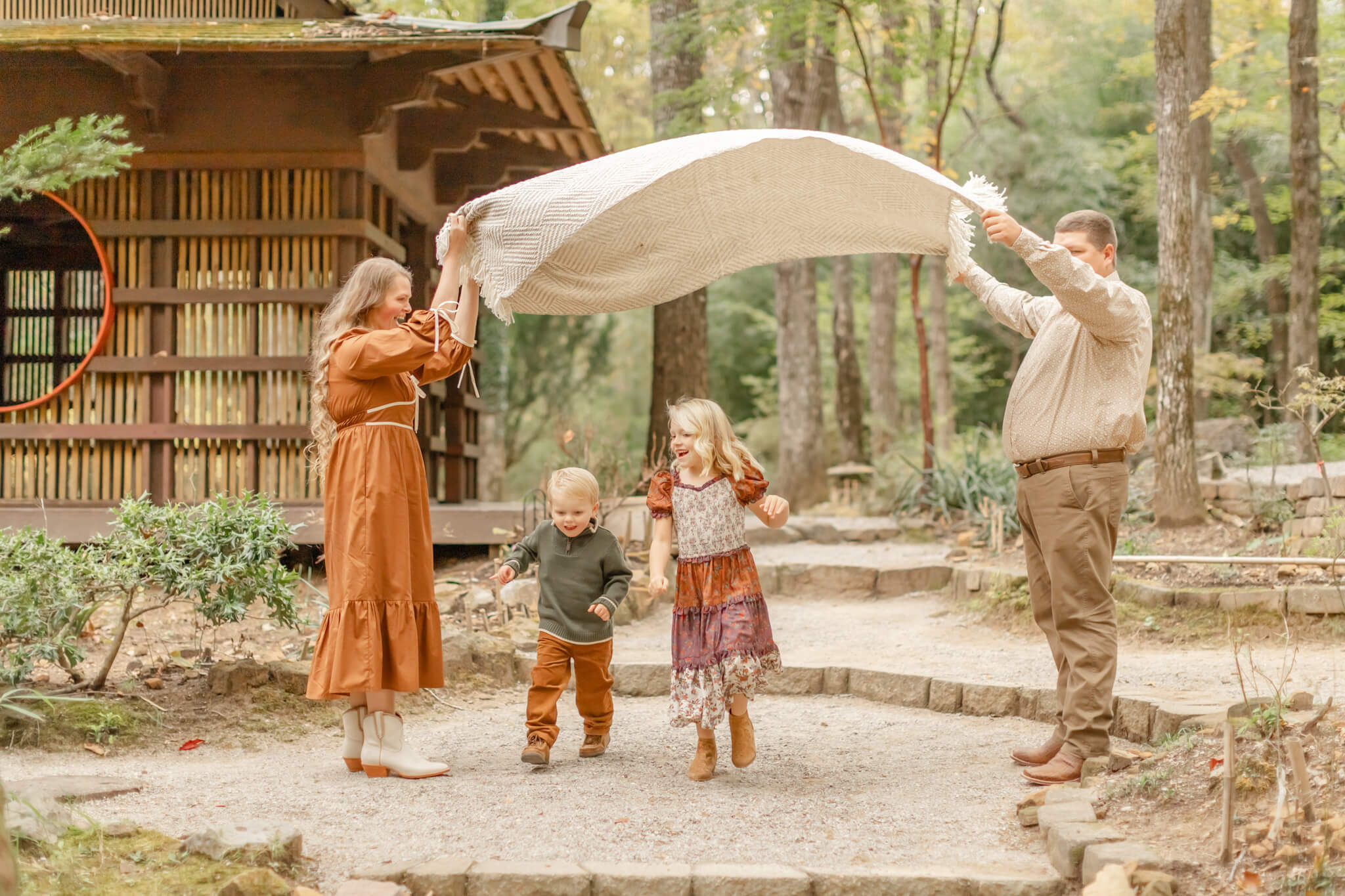 Toddler brother and sister dance and play under a blanket being lifted by mom and dad