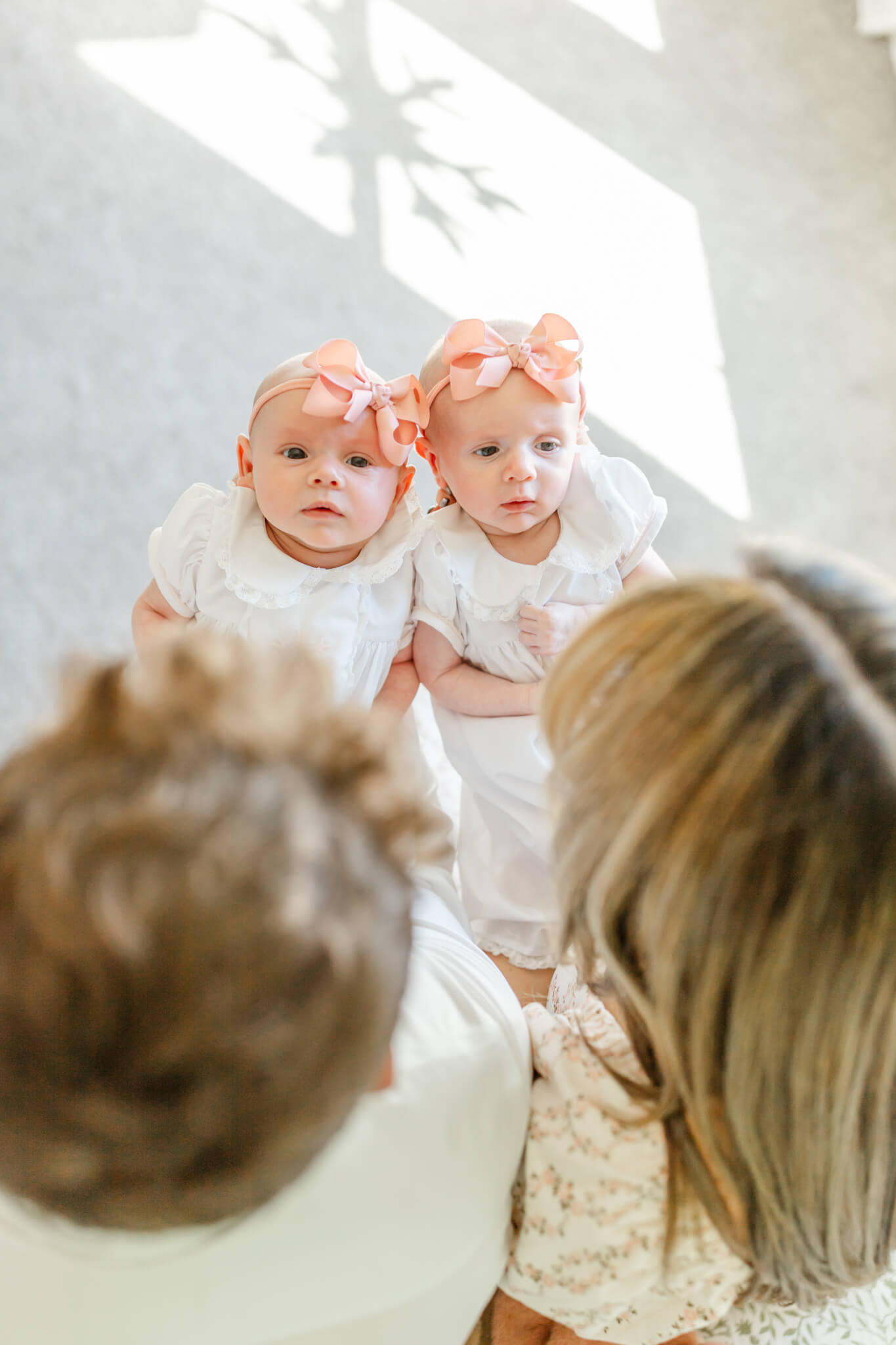 Newborn twin girls in white dresses and pink bows laying in mom and dad's hands after meeting nannies in Huntsville, AL