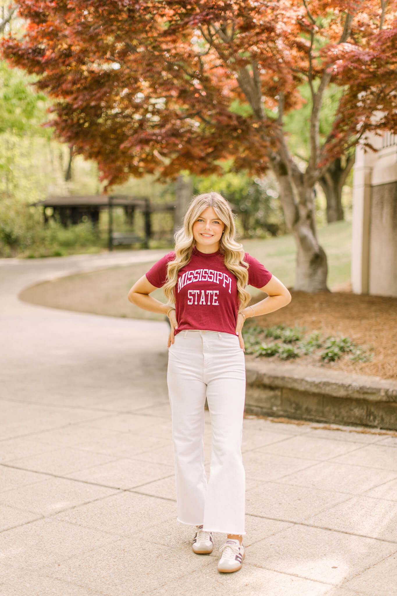 A high school senior stands in a garden path with hands on her hips in a college shirt after visiting great hair salons in Huntsville, AL