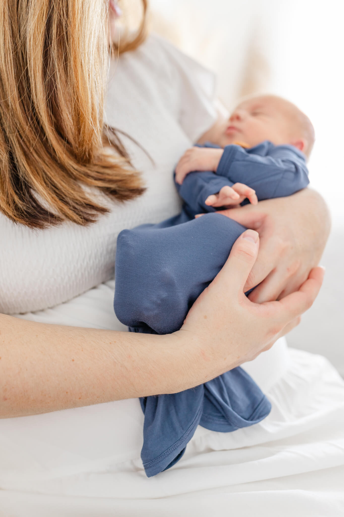 A sleeping newborn baby in a blue onesie in mom's arms