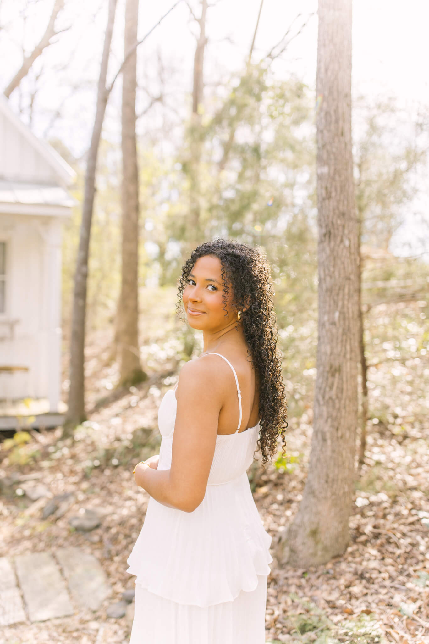 A high school senior smiles over her shoulder while exploring a garden in a white dress at sunset after finding perfect prom dresses in huntsville al