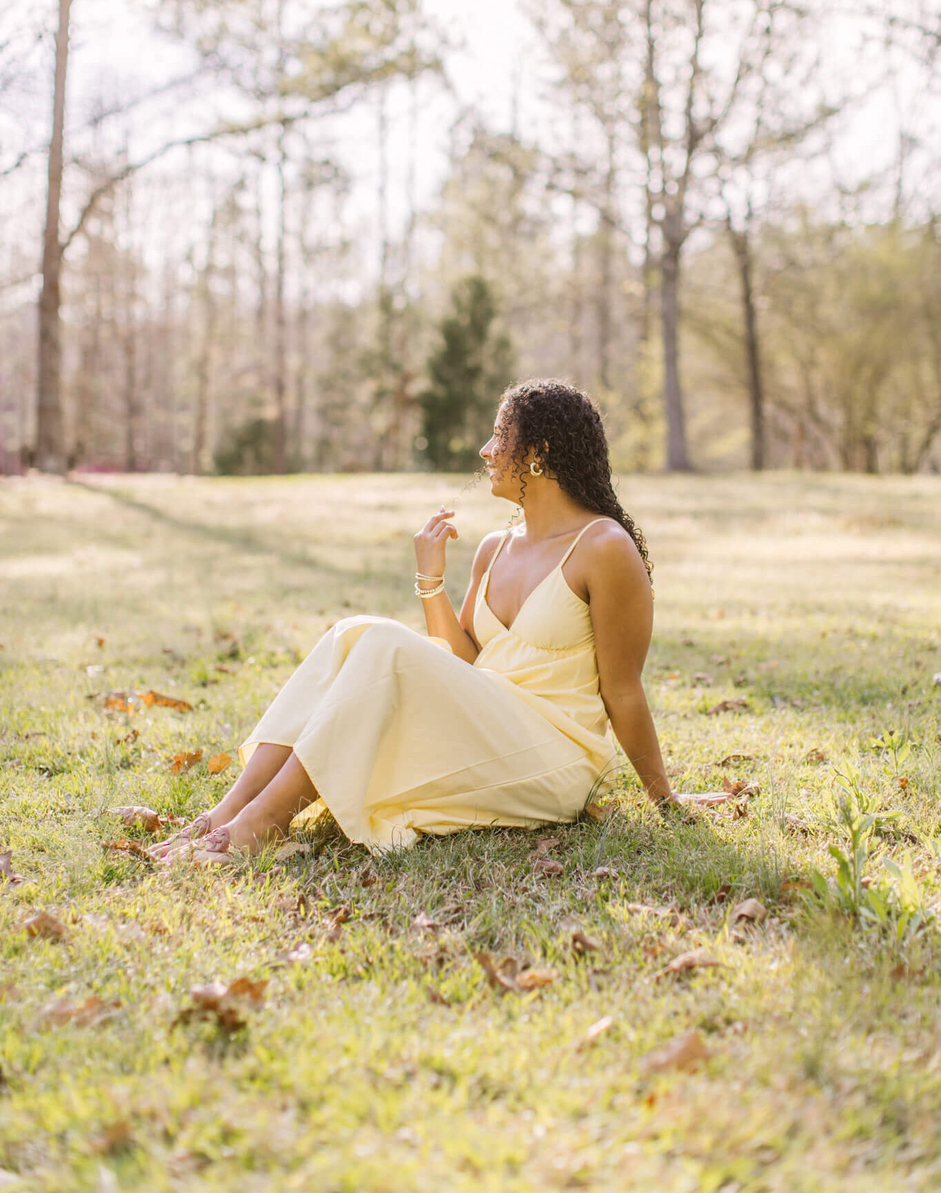 A happy high school senior lounges in a park in wearing a yellow dress with big smiles after visiting nail salons in Huntsville, AL