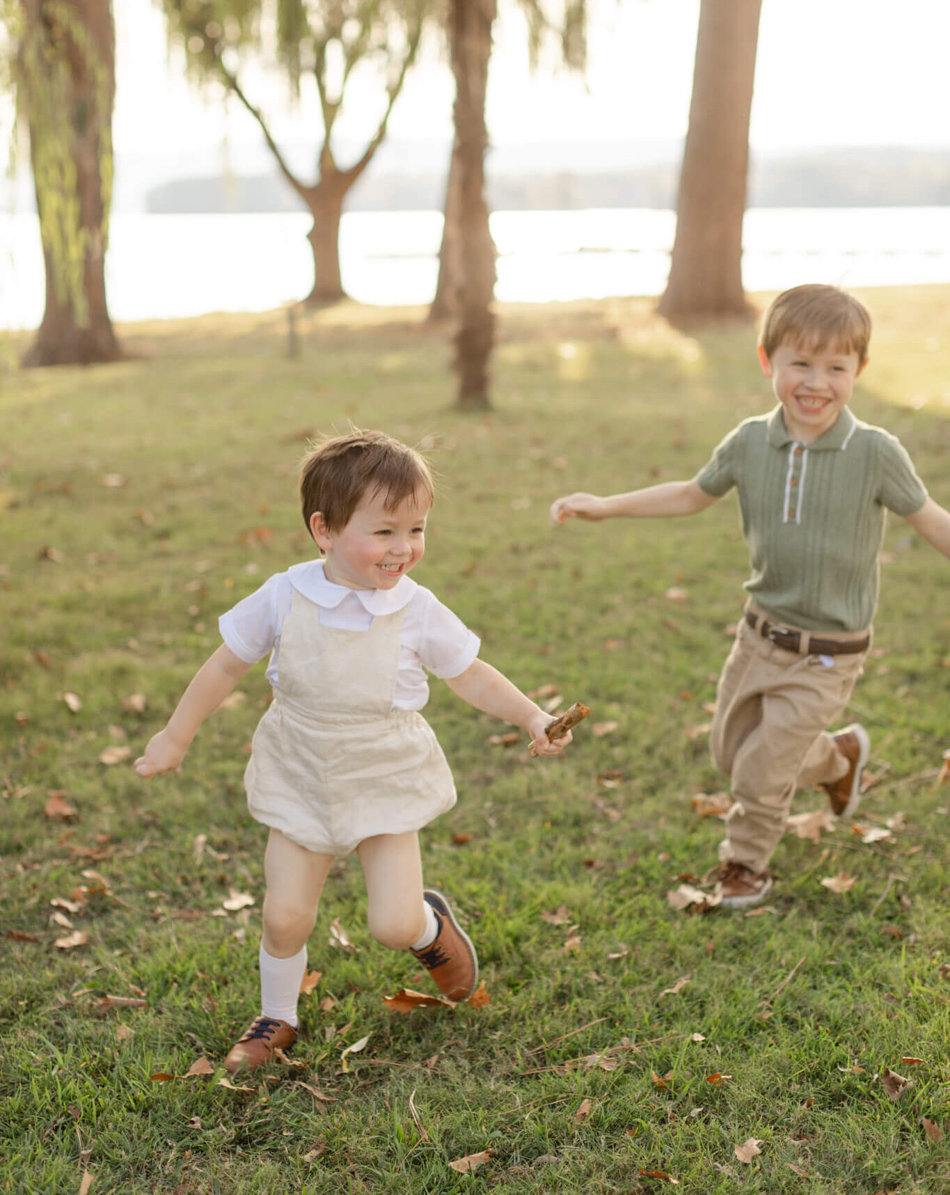Toddler siblings chase each other in a park at sunset by a lake in green and yellow after finding daycares in huntsville al