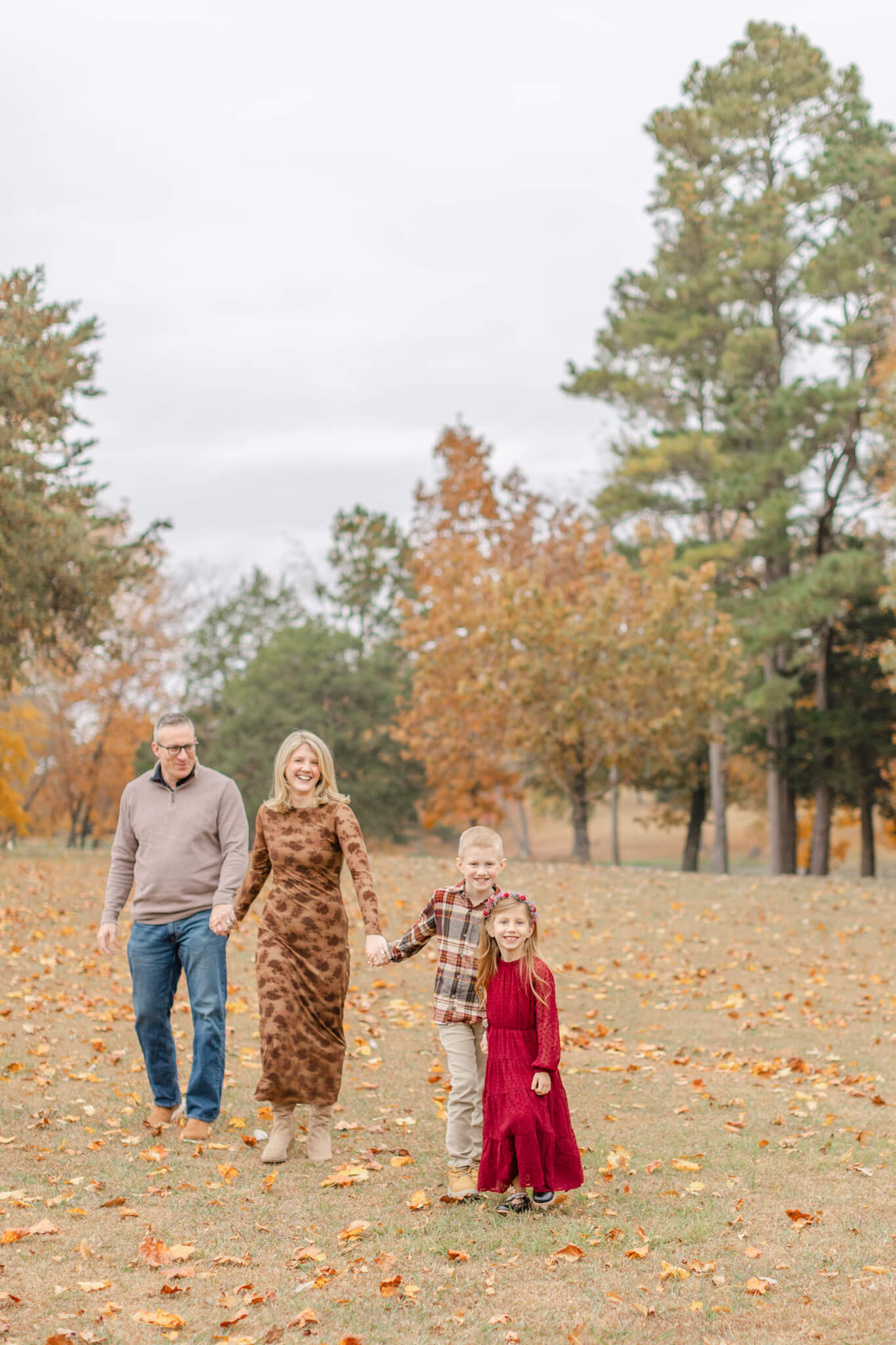 a happy family of four walk holding hands in a park lawn in fall