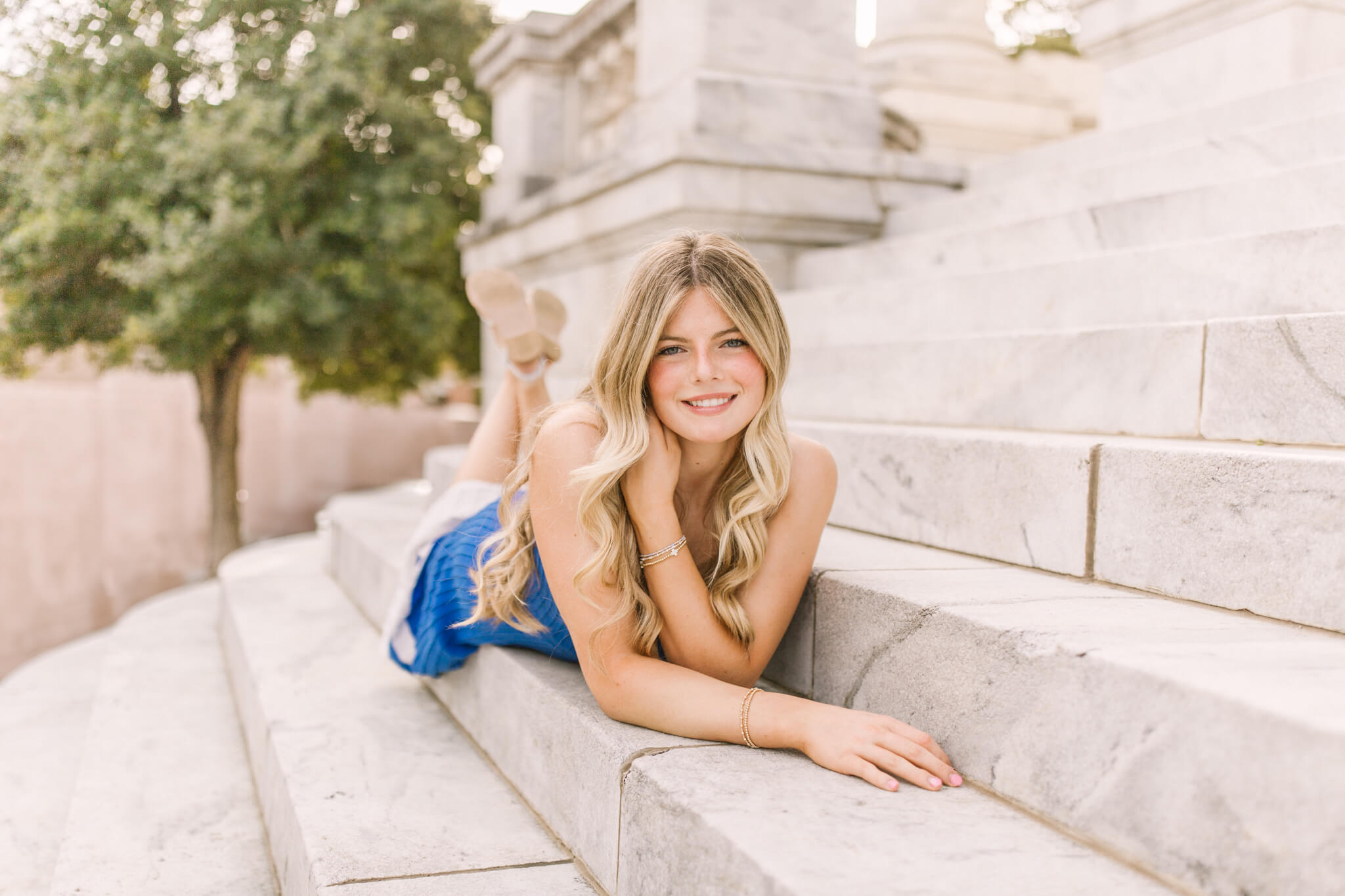 A high school senior in a blue dress lays across marble steps outdoors after finding great sat prep in Huntsville, AL