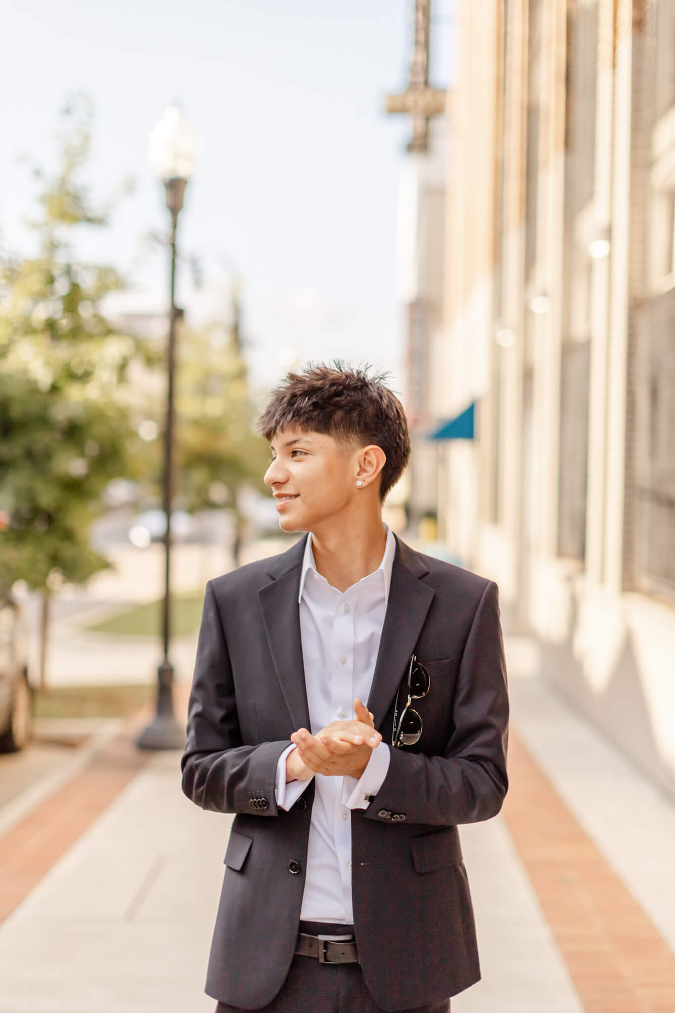 A clapping high school senior walks on a downtown sidewalk in a grey suit after finding perfect tuxedos in Huntsville, AL for prom