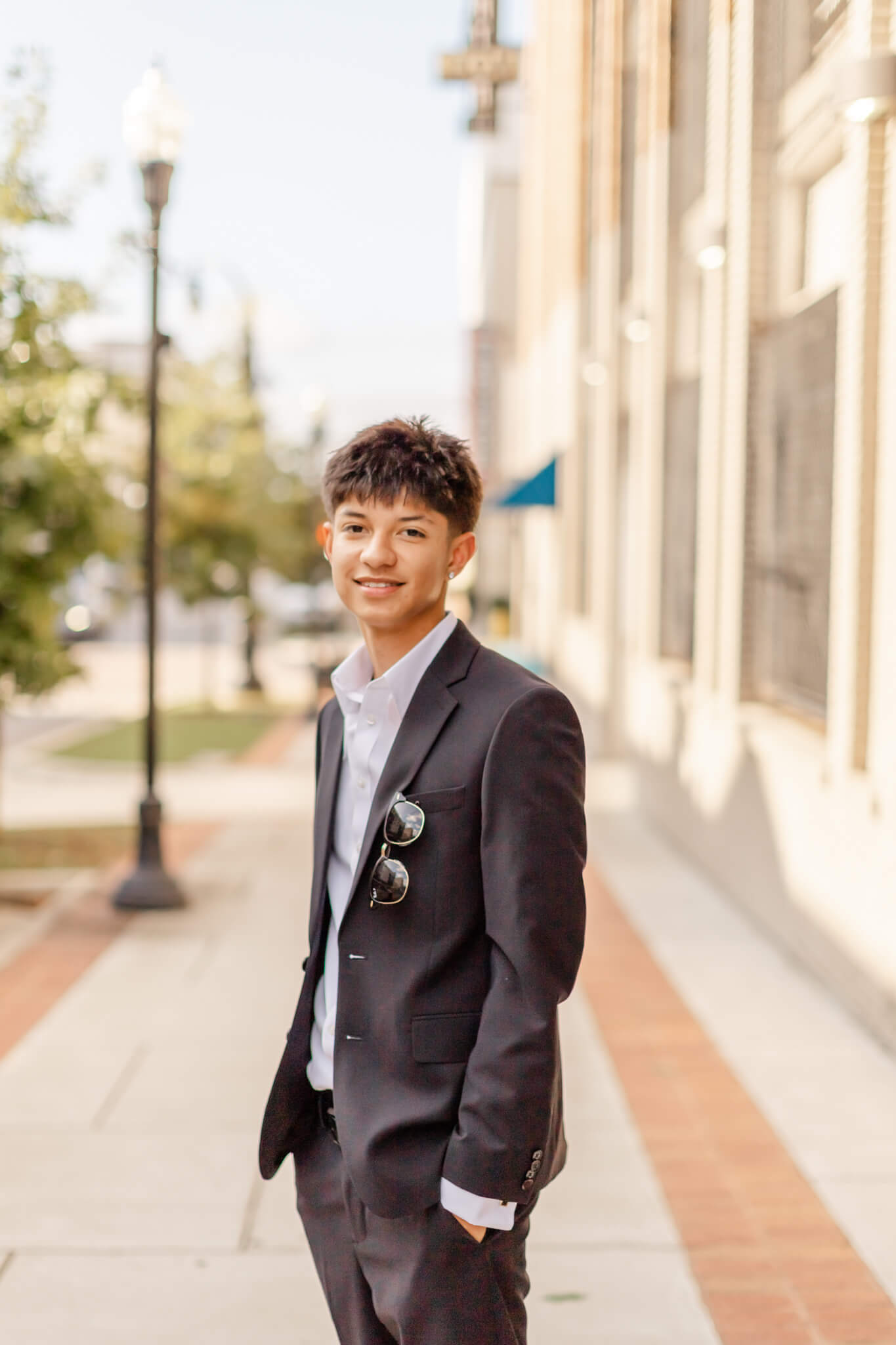 A high school senior stands with hands in pockets on a sidewalk smiling in a grey suit after finding tuxedos in Huntsville, AL for prom