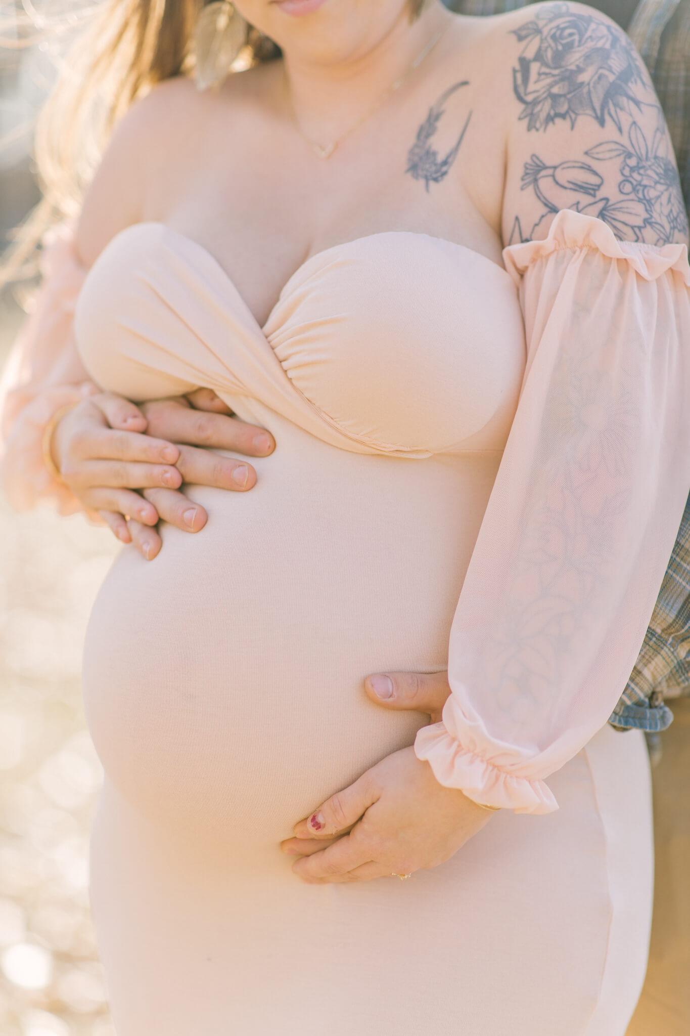 Details of a mother to be's bump in a pink maternity gown with her and husband's hands on it