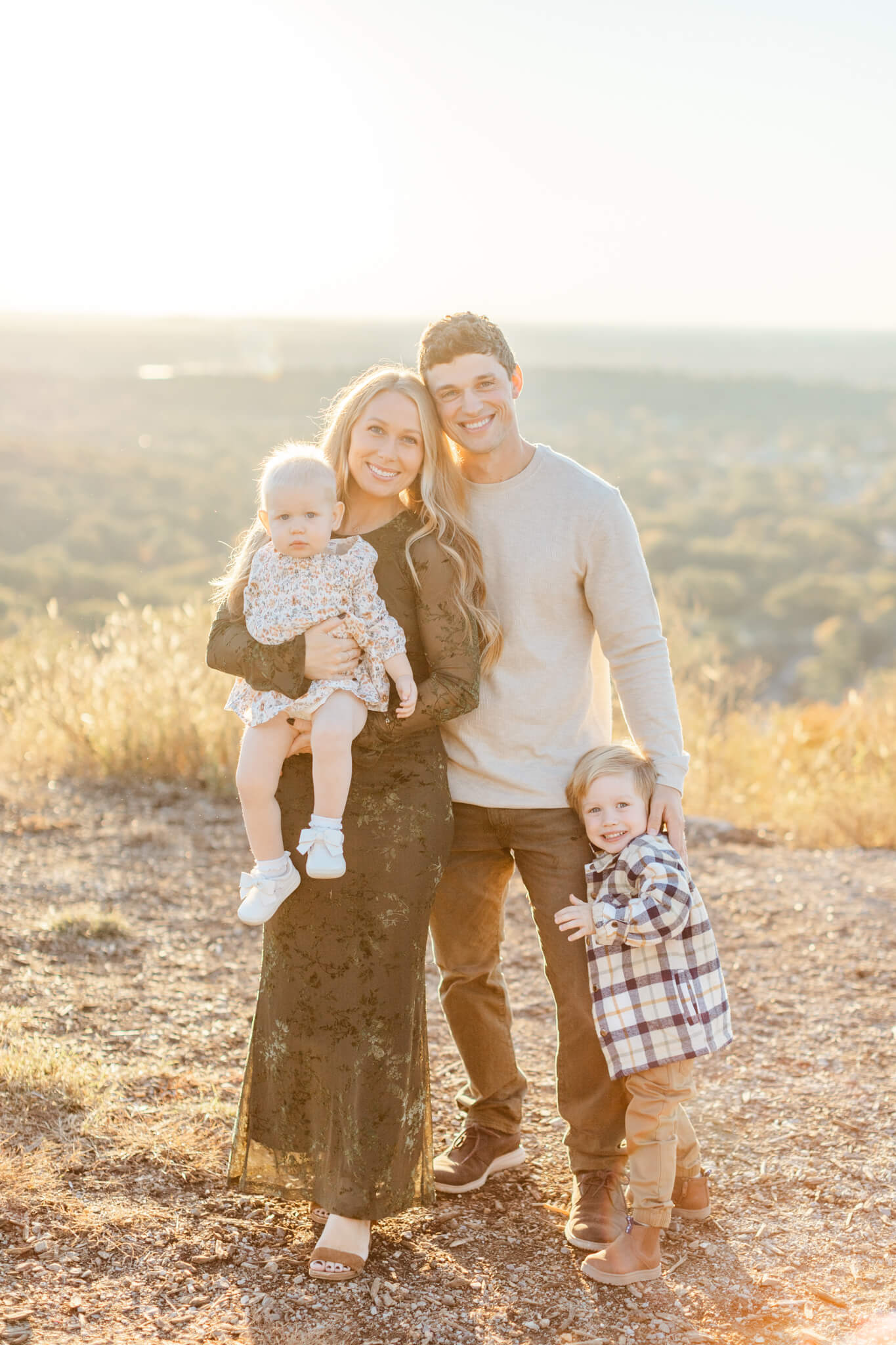 A mom and dad stand on an overlook smiling and holding heir toddler son and daughter
