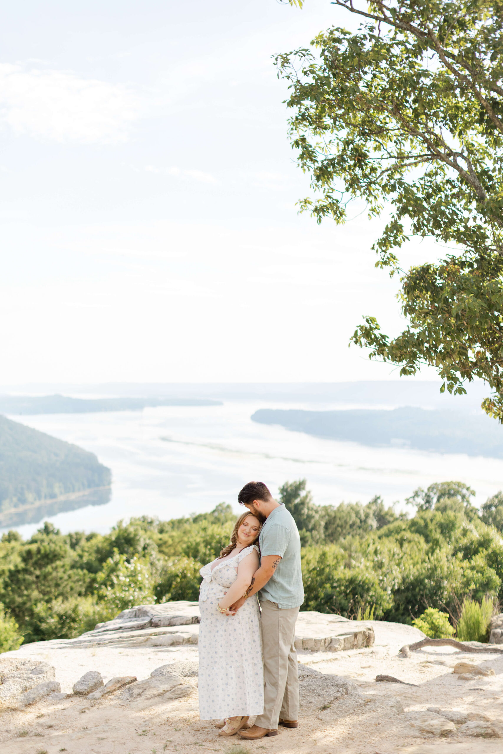 A happy expectant couple snuggles on an epic river overlook after engaging with Know Mommy