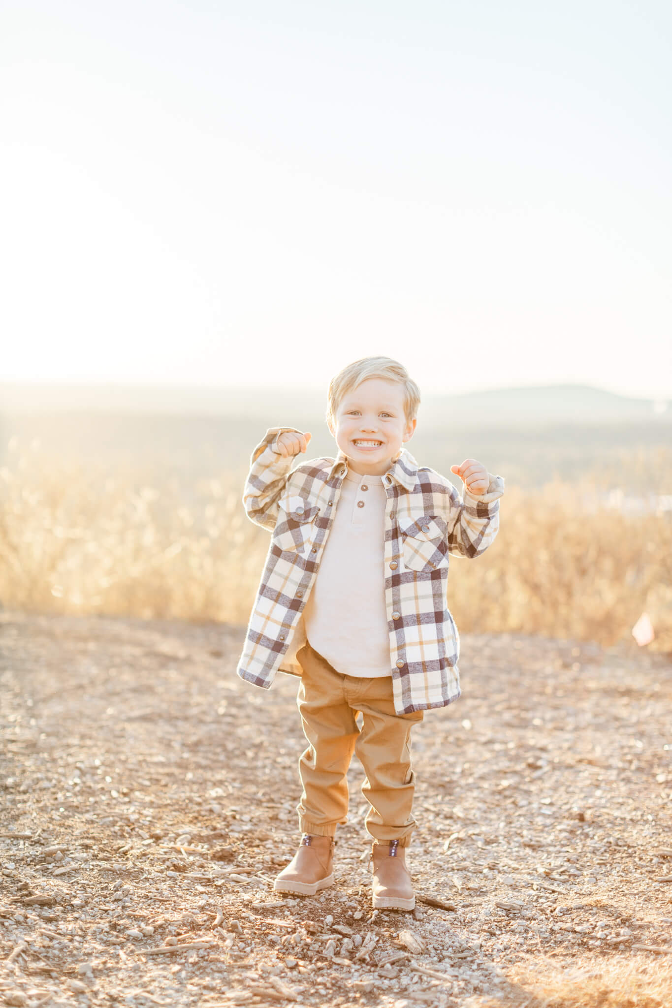 A happy toddler boy in a plaid shirt flexes his muscles and smiles at sunset after enjoying preschools in huntsville al