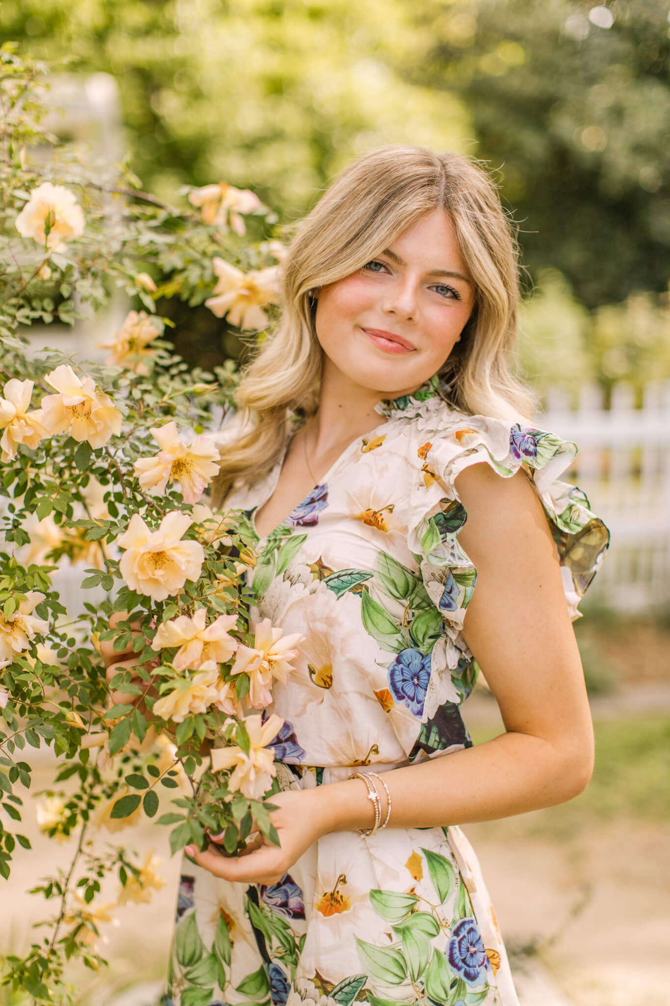 A smiling high school senior in a vibrant floral dress explires a flowering tree after finding tanning salons in huntsville al