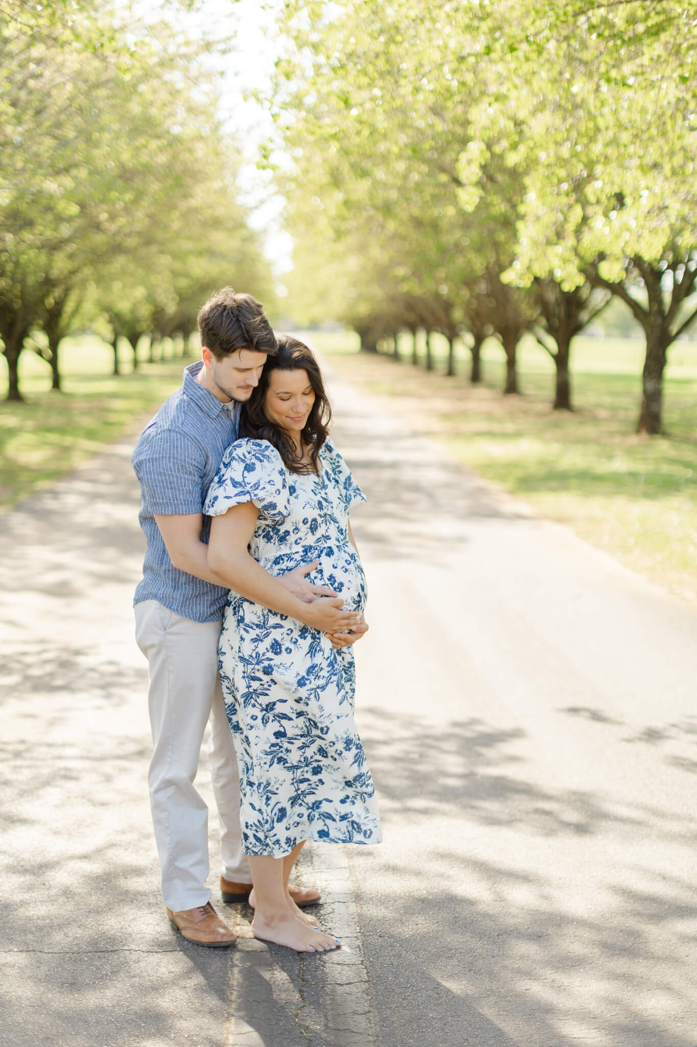 A happy pregnant couple snuggle the bump in blue outfits in a tree lined road after a 3d ultrasound in huntsville al
