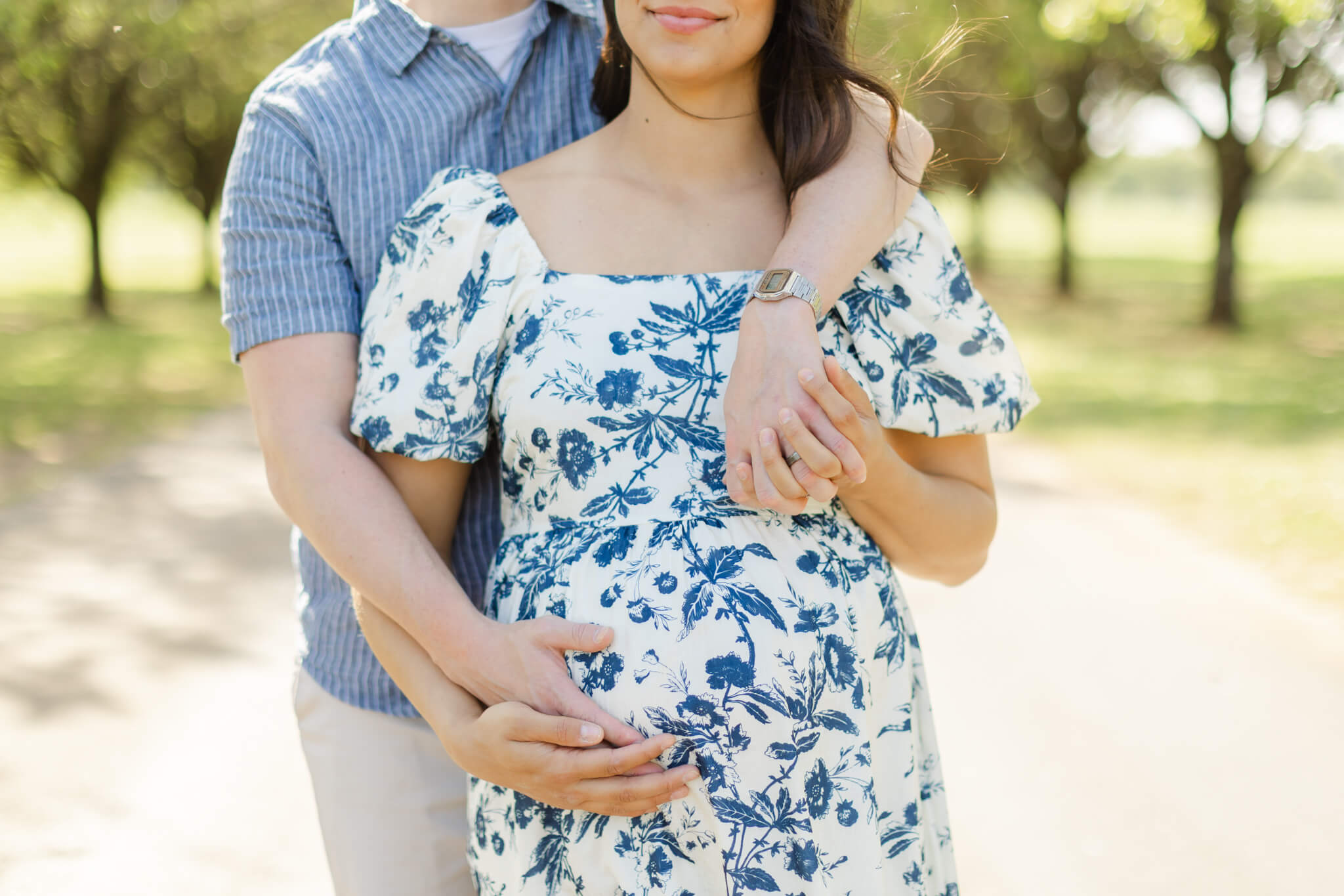 A mother to be snuggles her husband in a floral print maternity gown in a park after a 3d ultrasound in huntsville al