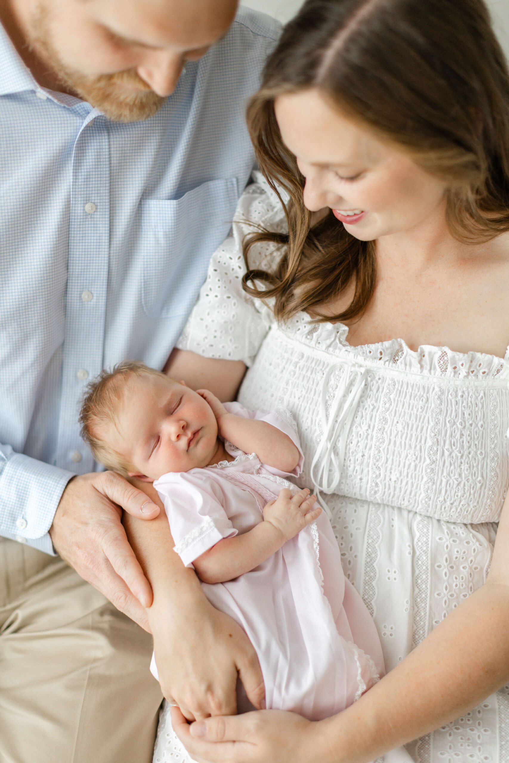 A newborn baby in a pink onesie sleeps in mom and dad's lap after mom explored The Bunny Hive Huntsville