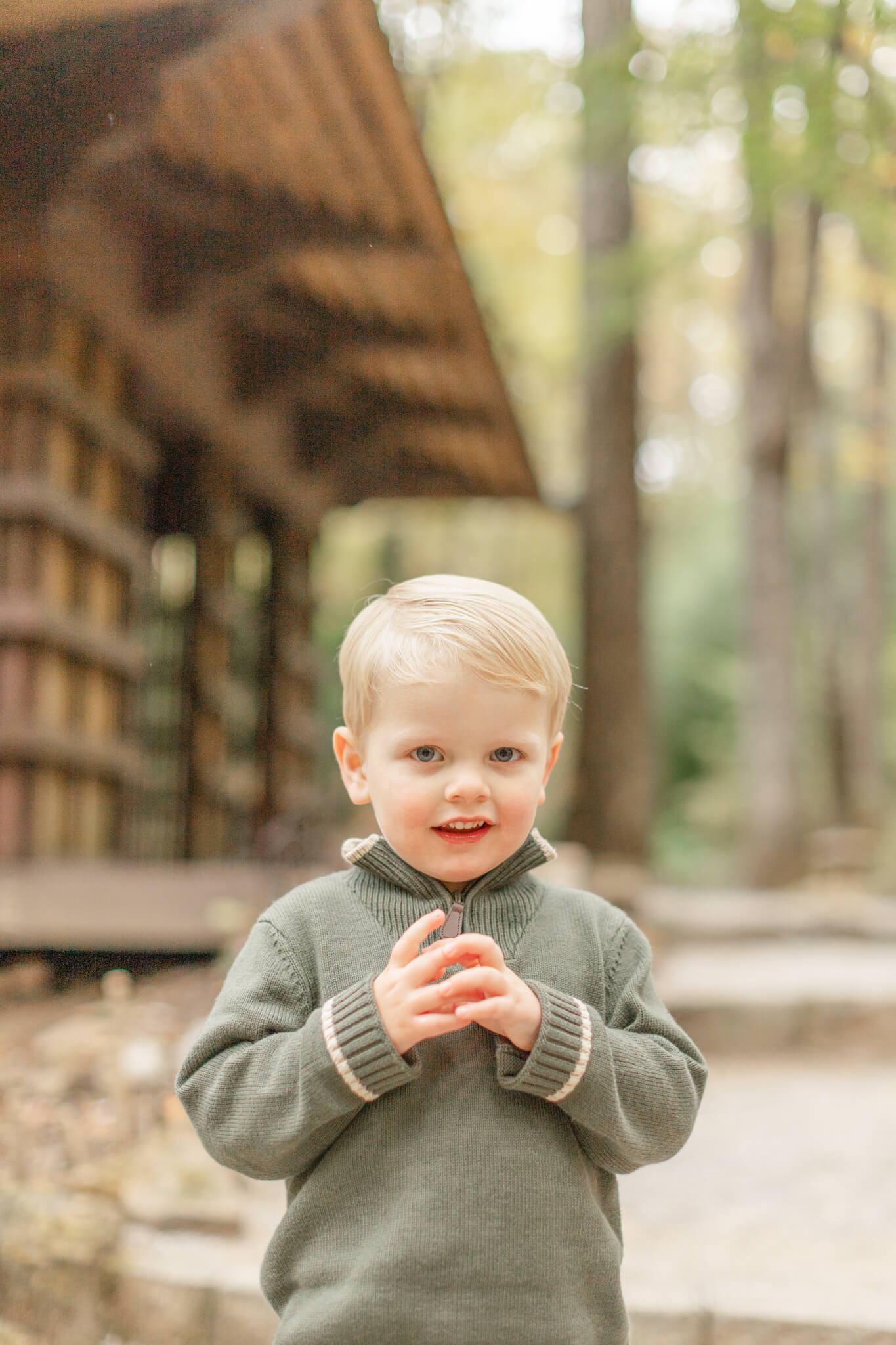 A young boy in a green sweater smiles in a forest after visiting children's boutiques in huntsville al