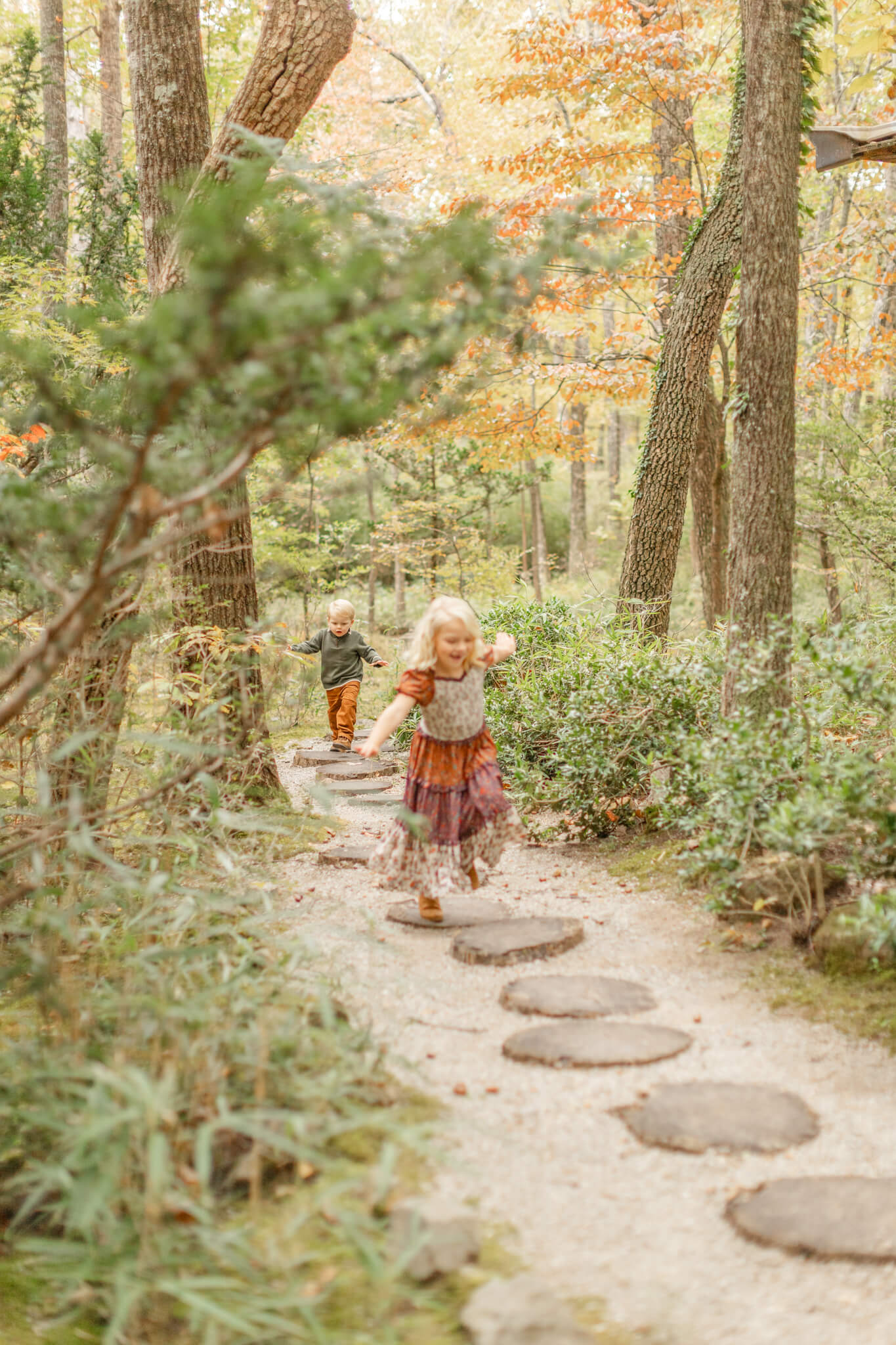 Toddler brother and sister run in a forest path after exploring children's boutiques in huntsville al