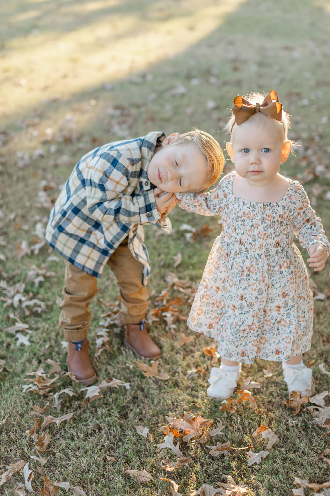 Toddler brother and sister in a park lawn at sunset in fall outfits
